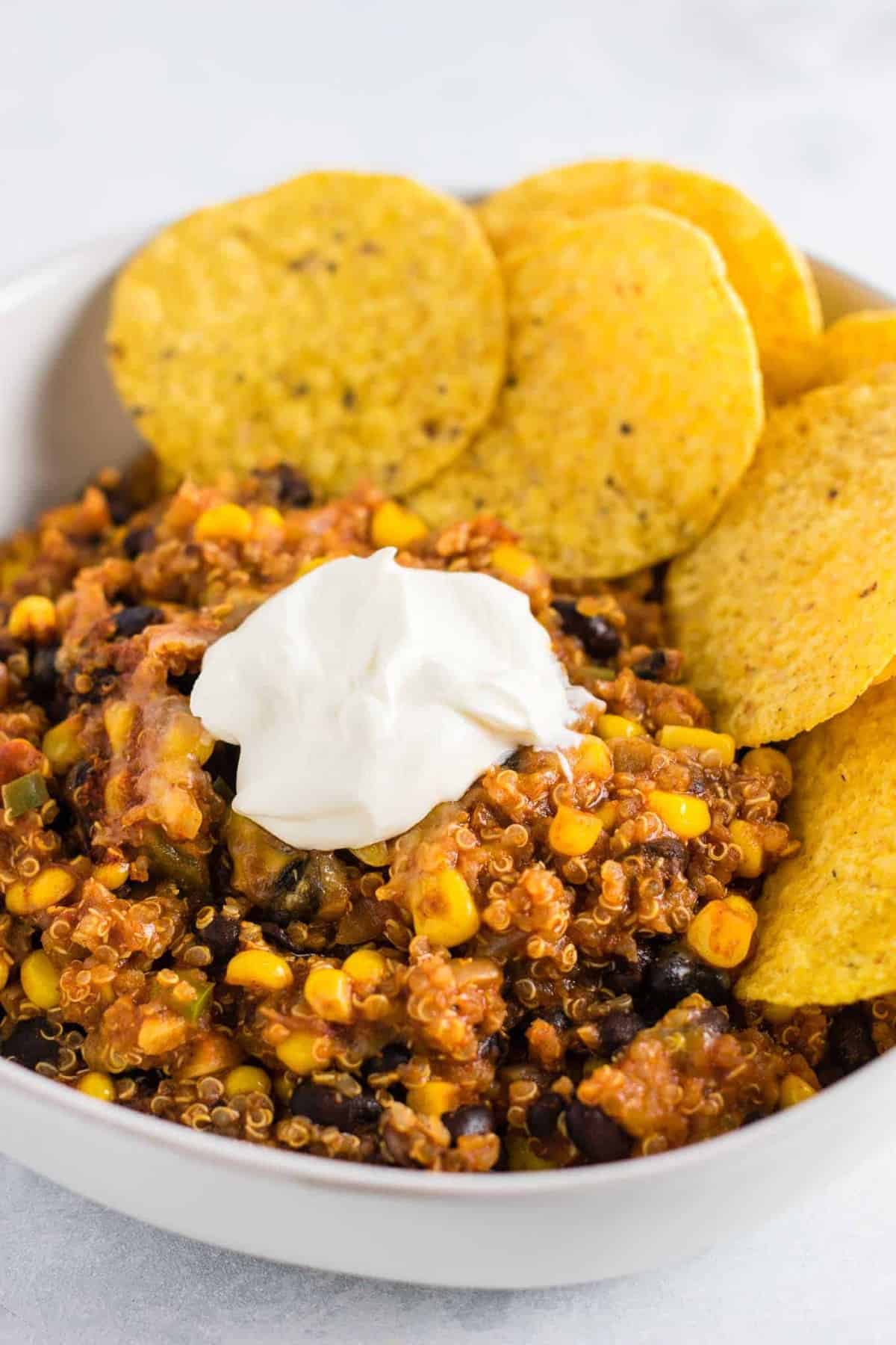 mexican quinoa enchilada bake in a bowl with sour cream and chips