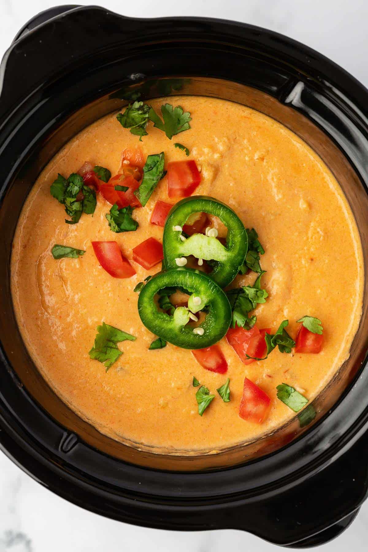 queso dip in a crock pot topped with pico and jalapeno slices