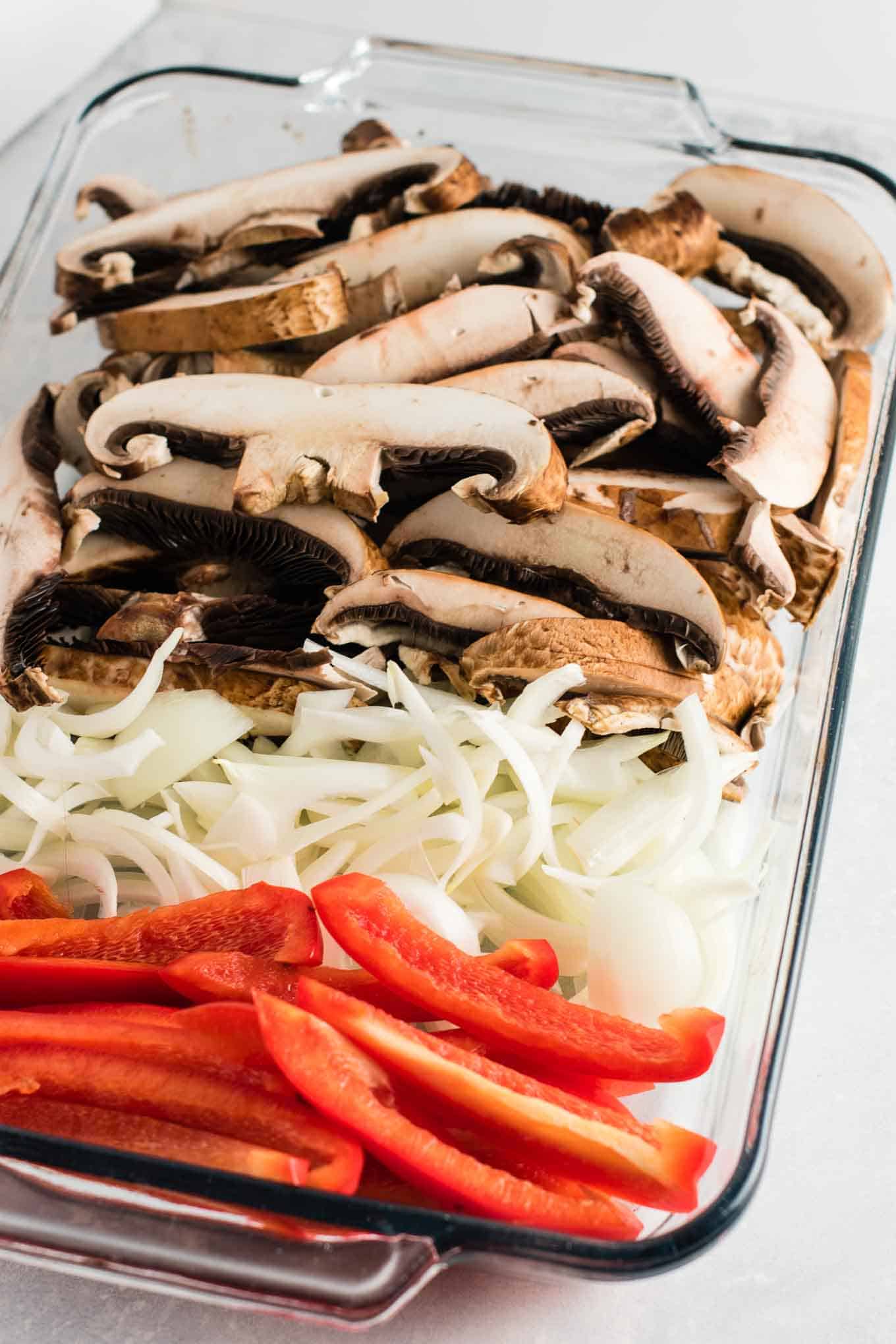 sliced portobello mushroom caps, onion, and red bell pepper in a glass baking dish