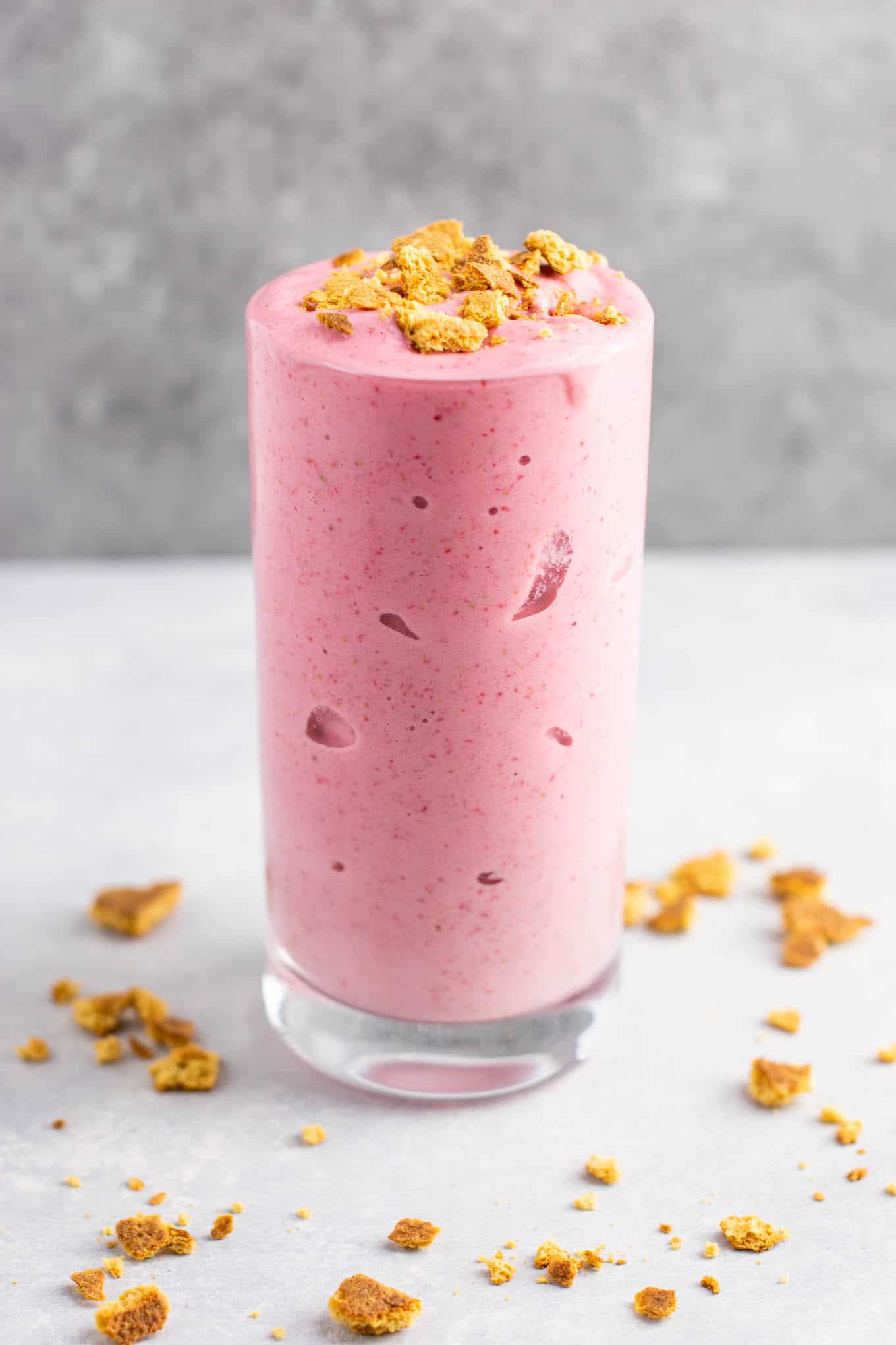 strawberry cheesecake smoothie in a glass with crushed graham cracker on top