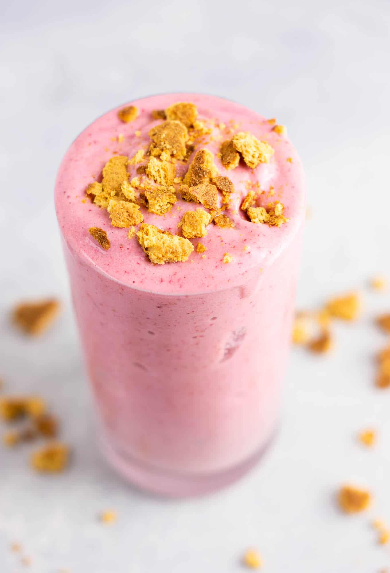 strawberry cheesecake smoothie in a glass with crushed graham cracker on top