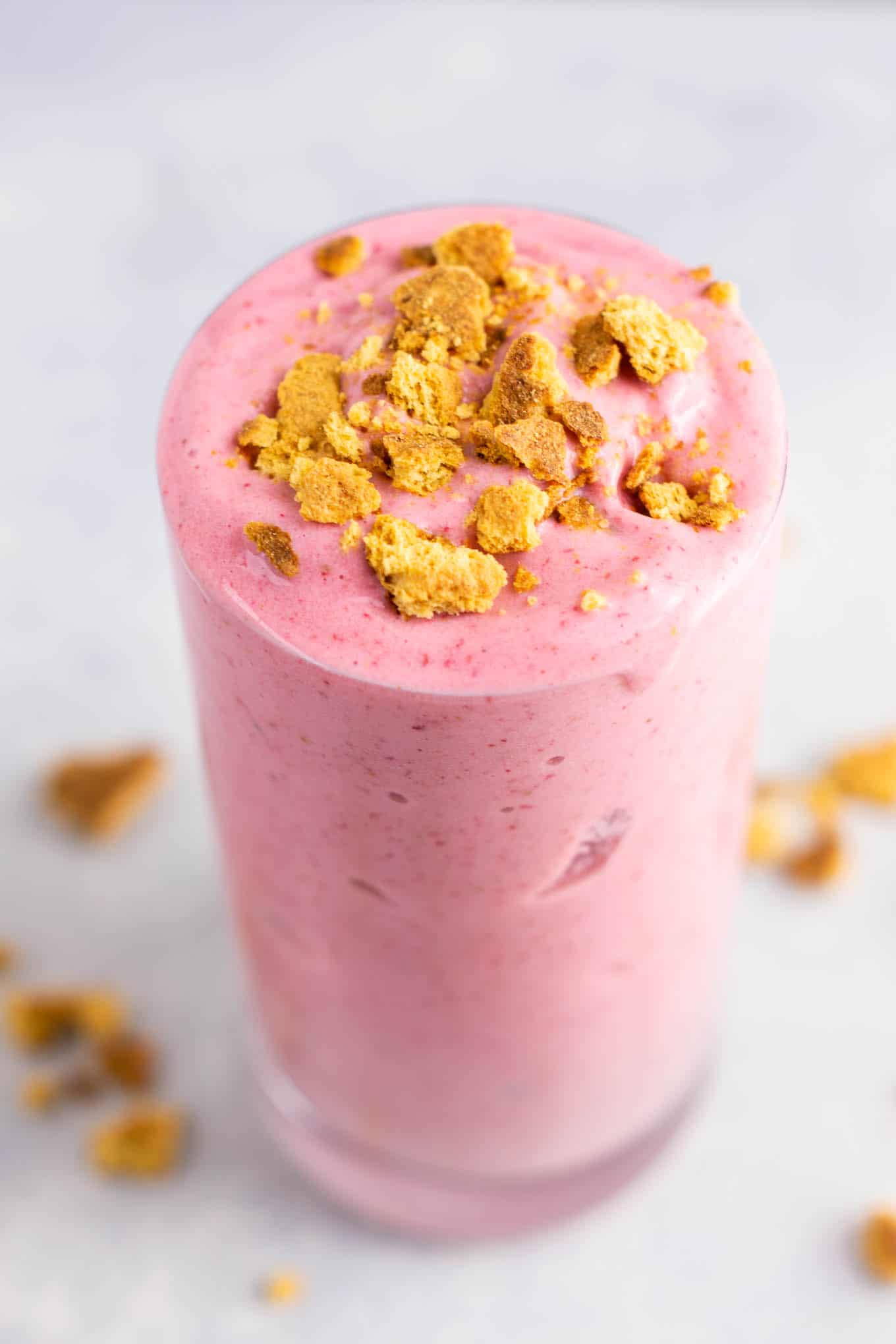 strawberry cheesecake smoothie in a glass with crushed graham cracker on top