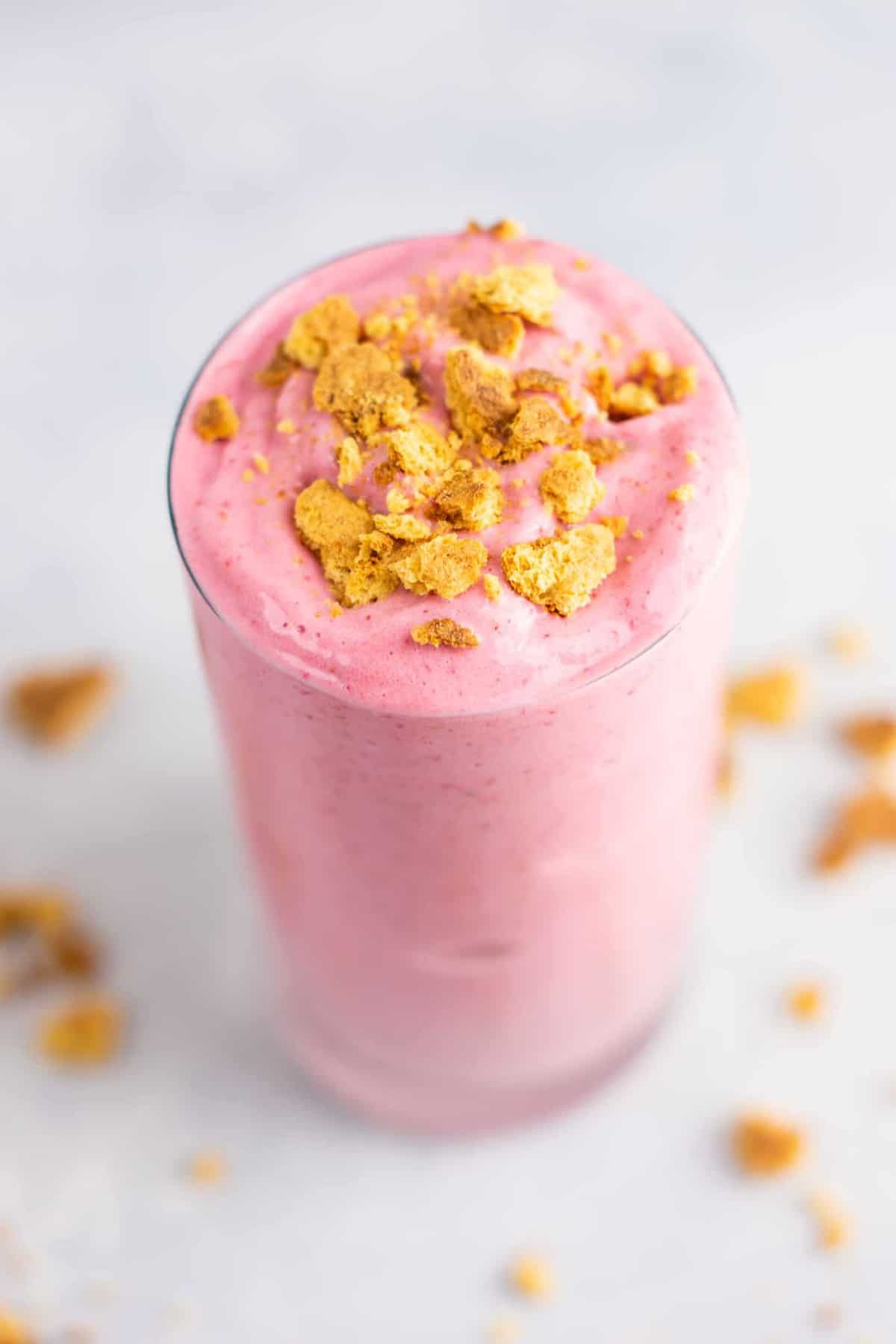 strawberry cheesecake smoothie in a glass topped with crushed graham crackers