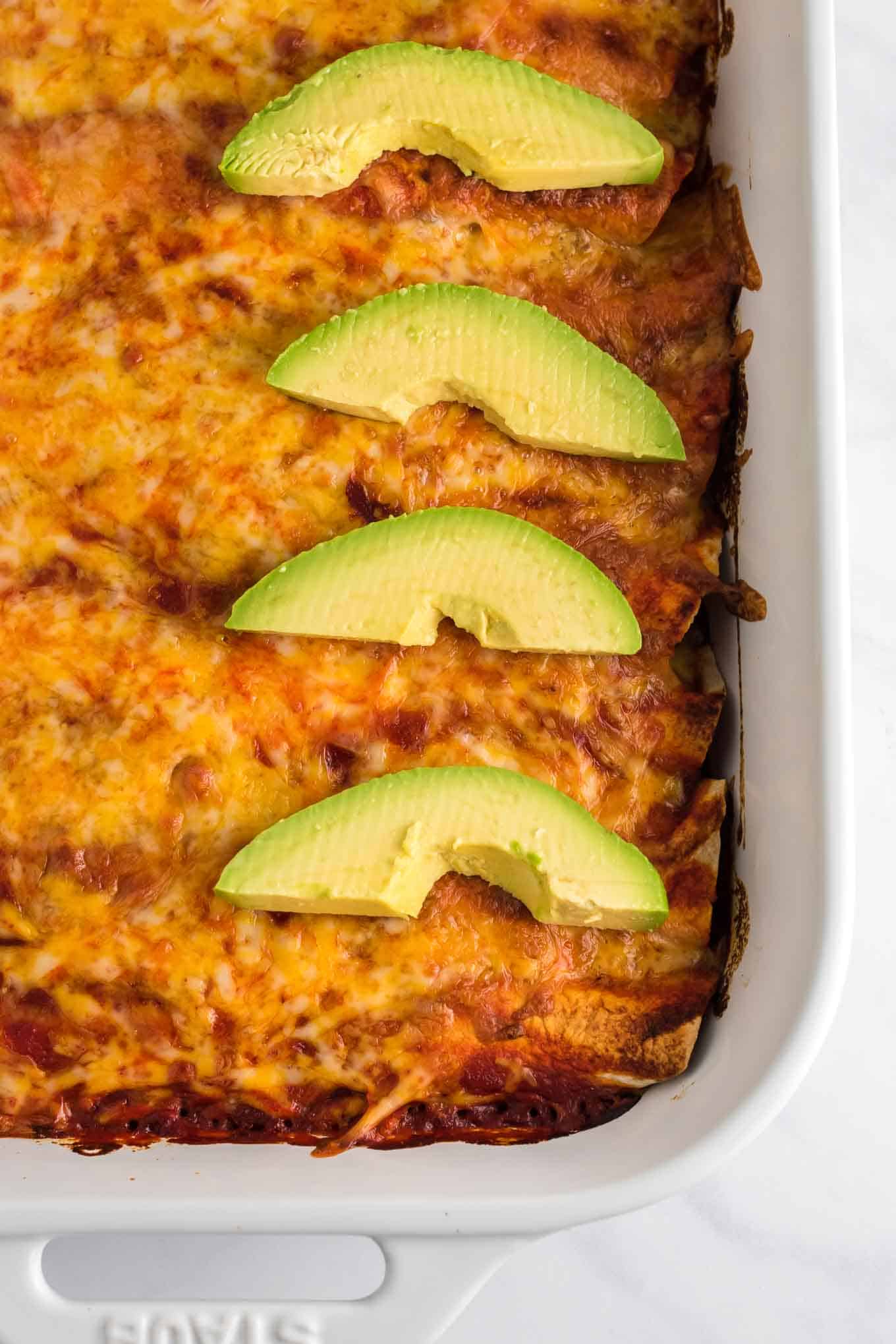 sweet potato black bean enchiladas from an overhead view with three slices of avocado on top