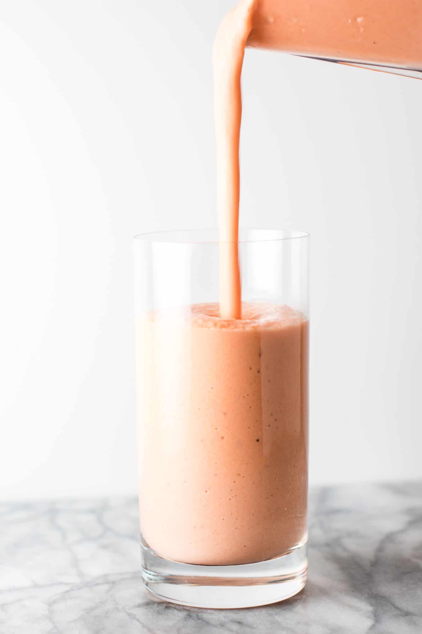 smoothie being poured into a glass from a blender, ¾ of the way full