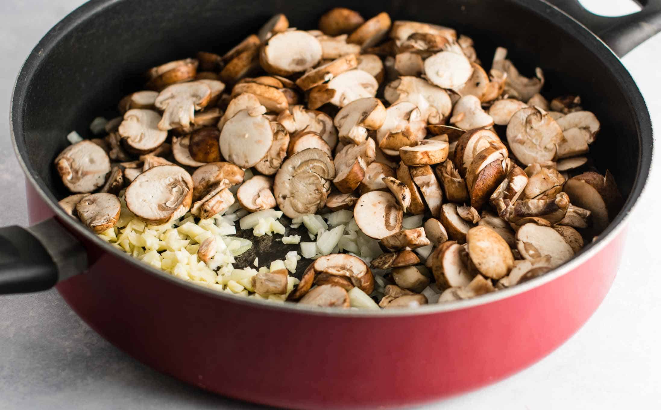 baby bella mushrooms, chopped onion, and minced garlic in a red skillet