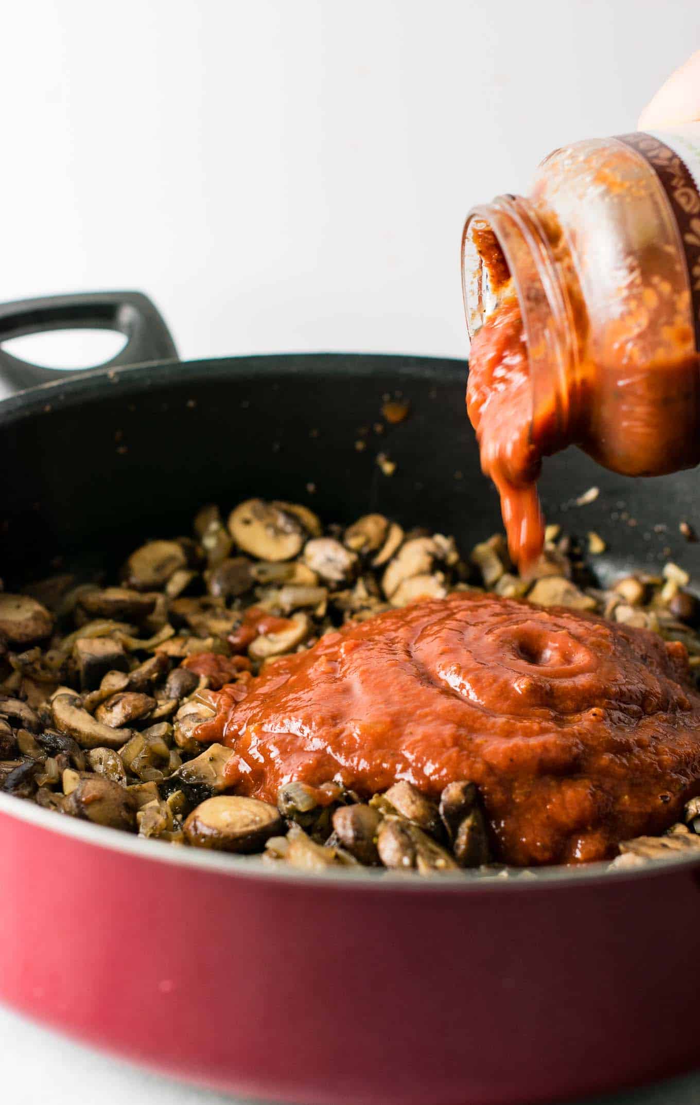 pasta sauce being poured into the skillet with the mushrooms