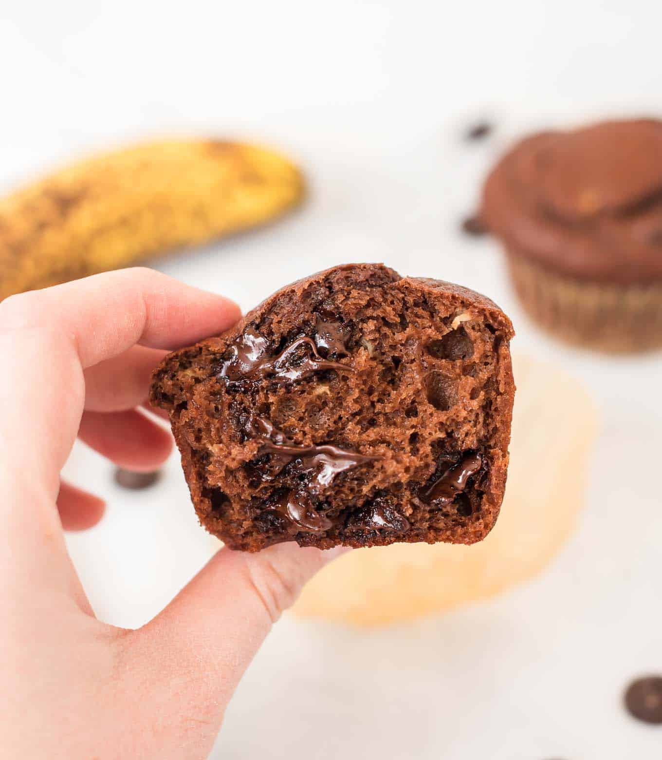 a hand holding half of a chocolate muffin to show the inside texture