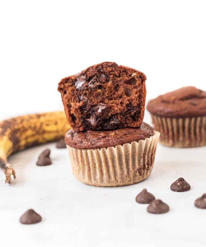 a chocolate muffin with a bite taken out stacked on top of another muffin