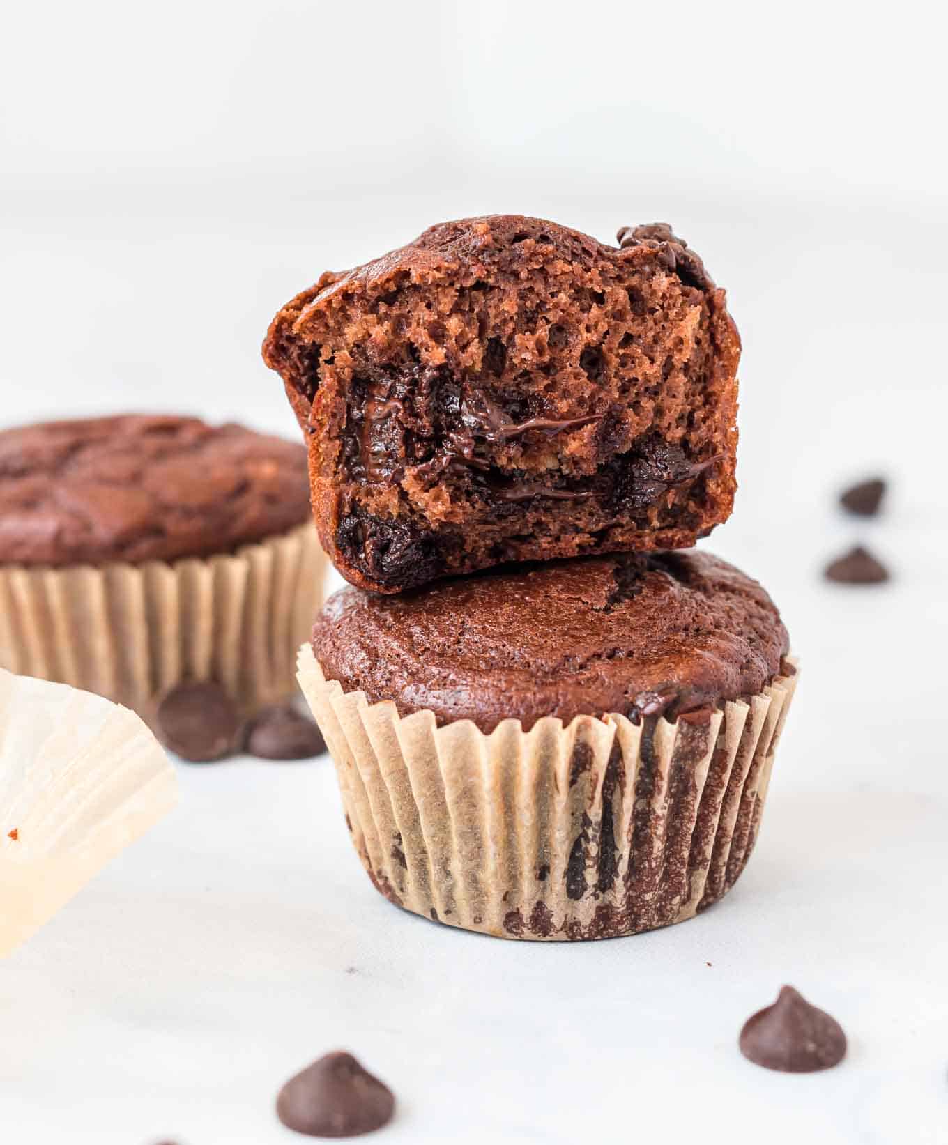 a chocolate muffin with a bite taken out stacked on top of another muffin