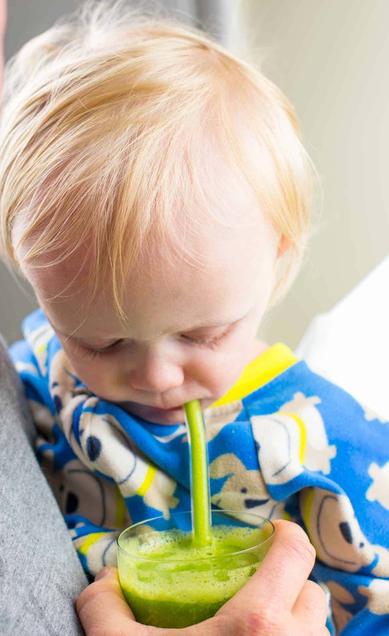 toddler taking a drink of green smoothie from a glass