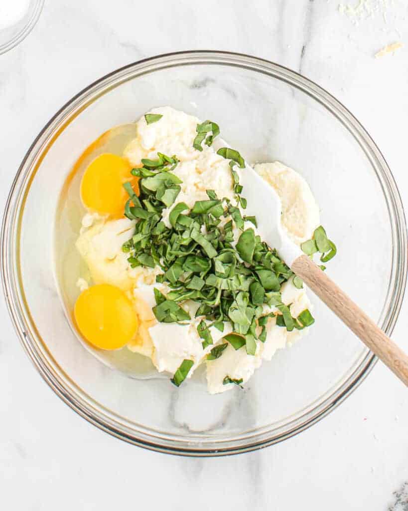 mixing together basil, ricotta, and eggs in a bowl