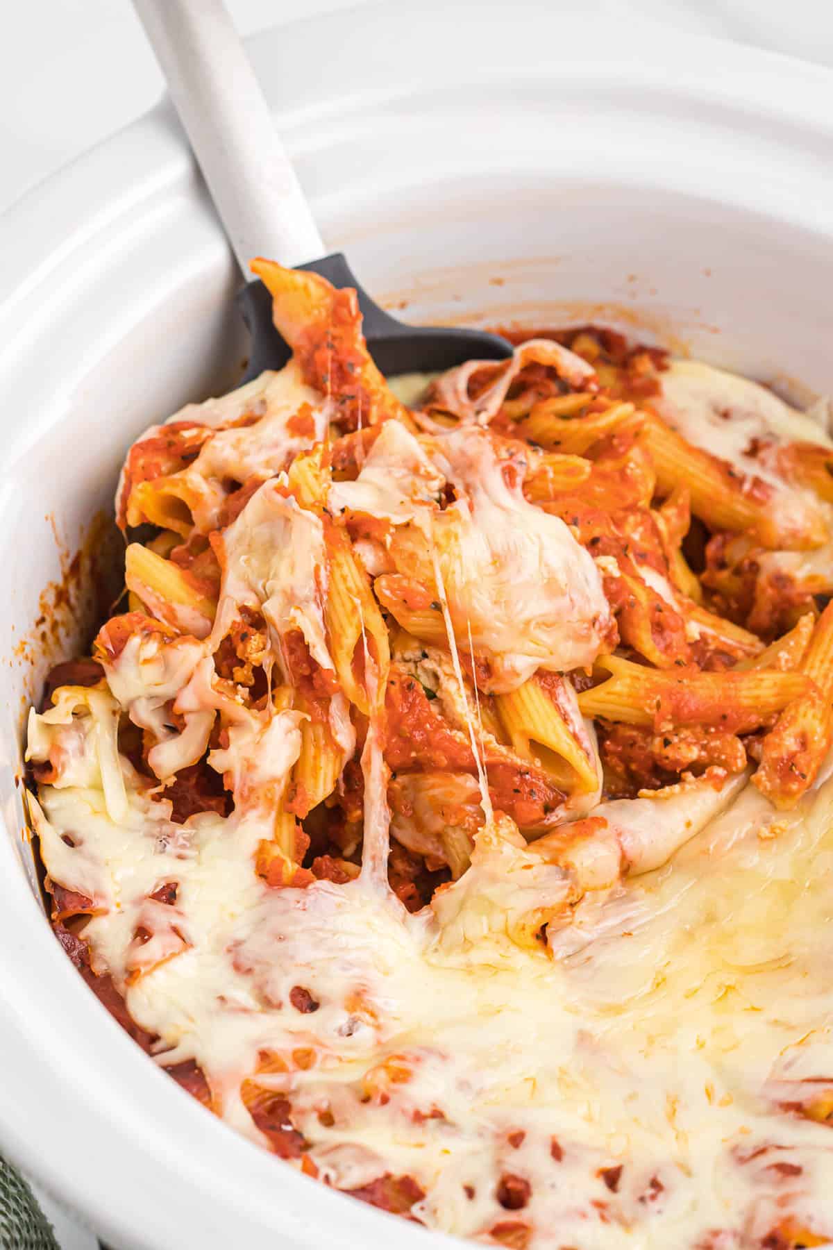 taking a scoop of baked ziti from the crock pot