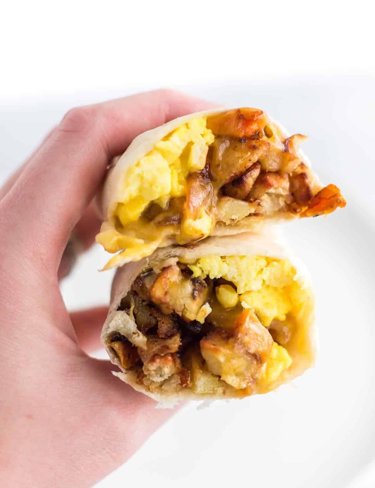 a hand holding a breakfast burrito cut open