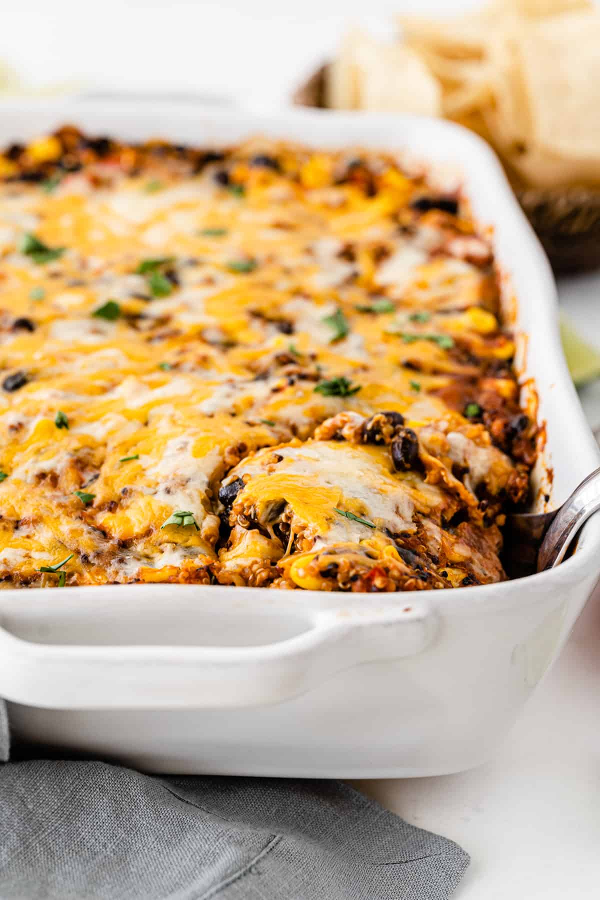 mexican quinoa casserole in a white baking dish with a spoon taking a scoop