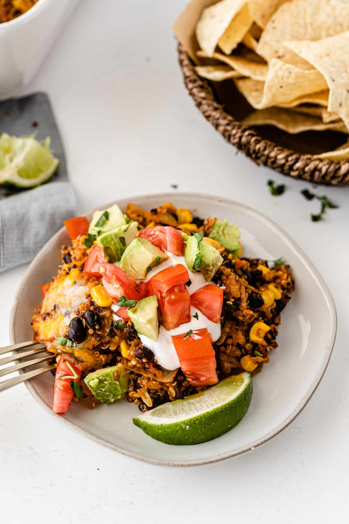 quinoa enchilada casserole on a white plate topped with sour cream, tomato, avocado, and lime