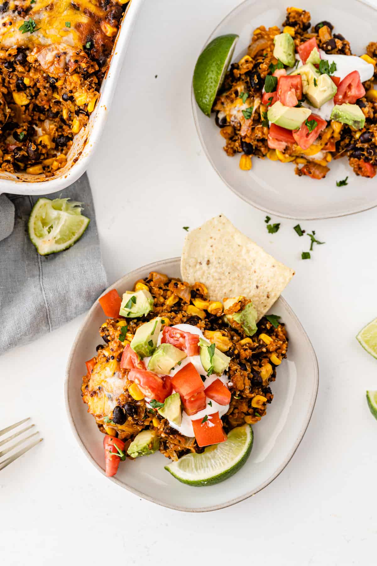 quinoa enchilada casserole on a white plate topped with sour cream, tomato, avocado, and lime