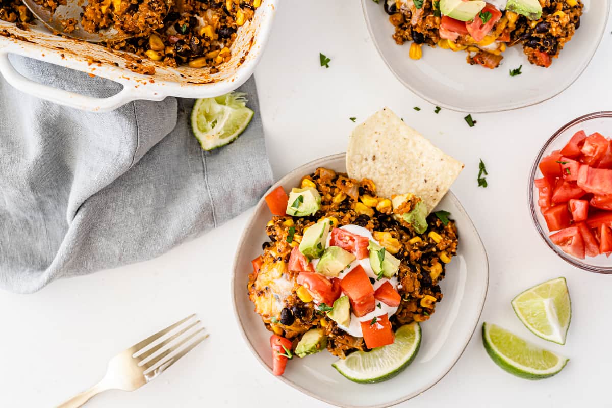 quinoa enchilada casserole on a white plate topped with sour cream, tomato, avocado, and lime