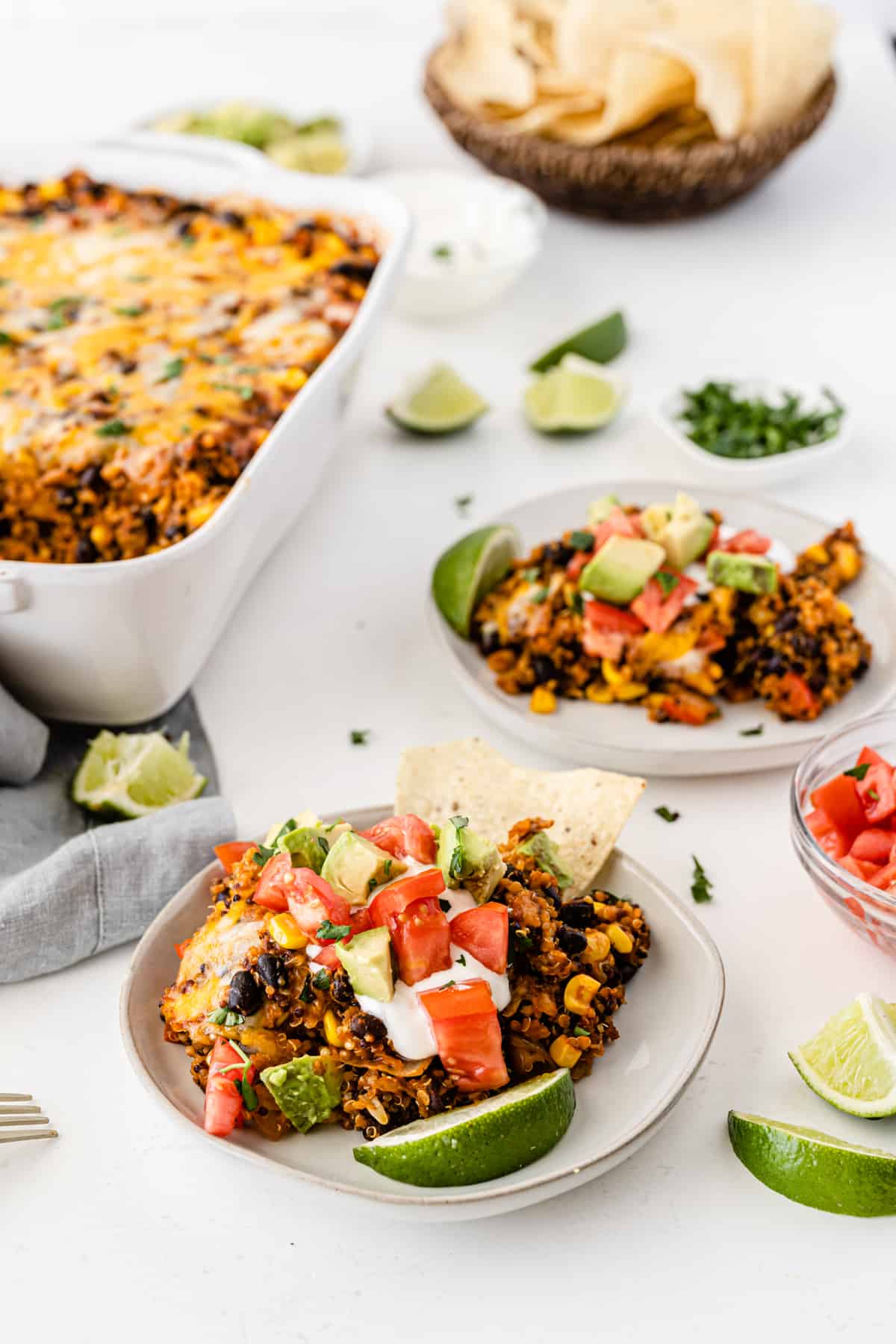 quinoa enchilada casserole on a white plate topped with sour cream, tomato, avocado, and lime