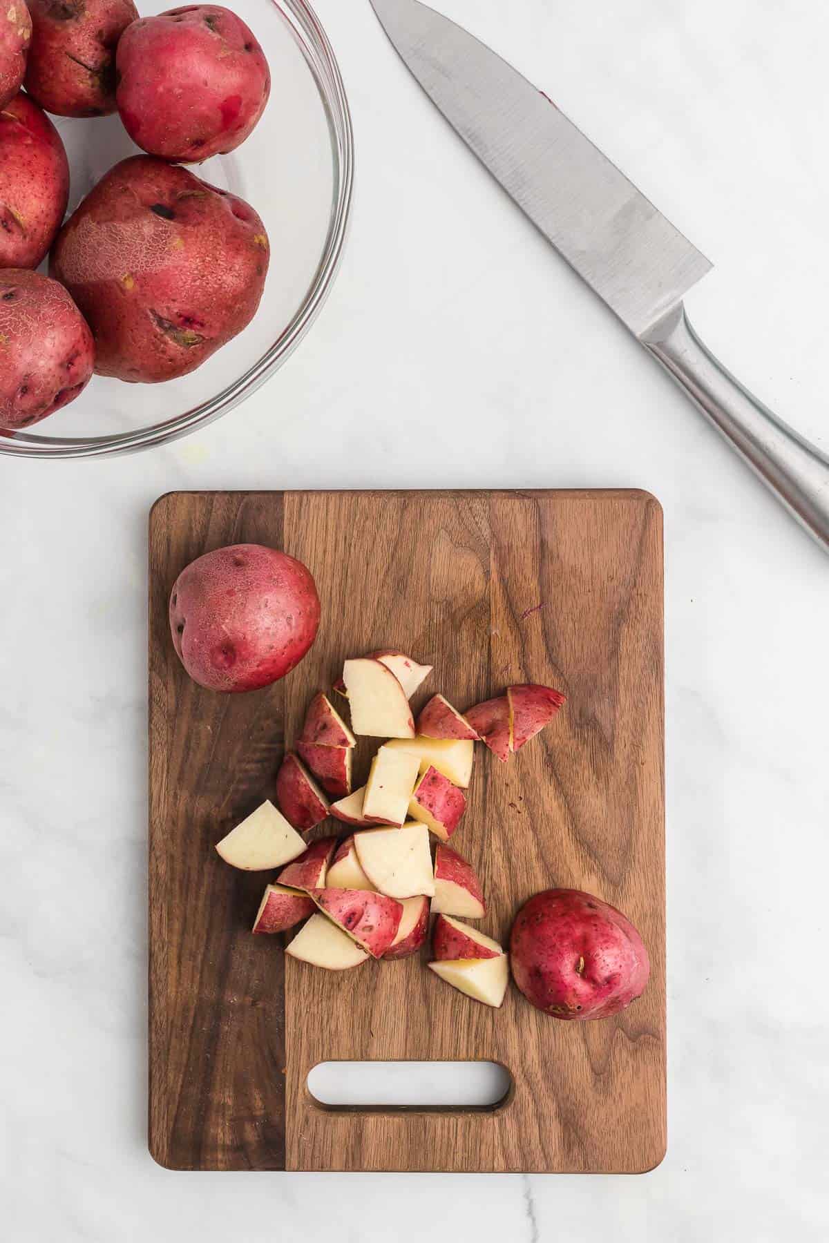 cutting red potatoes into chunks on a cutting board