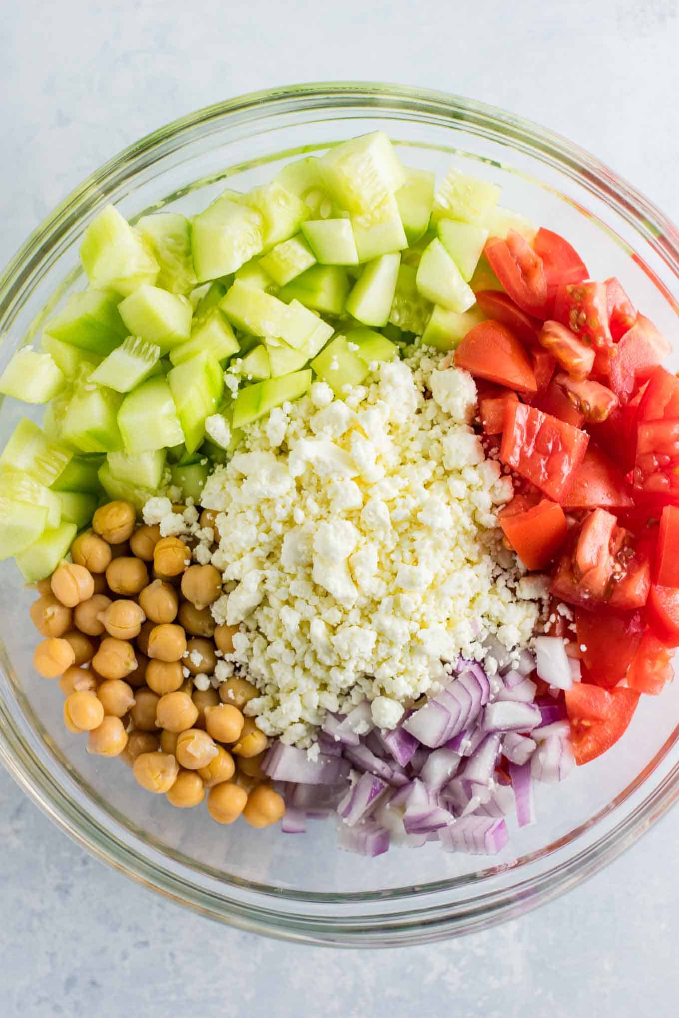 ingredients in a bowl before mixing - cucumbers, feta cheese, red onion, tomatoes, and chickpeas