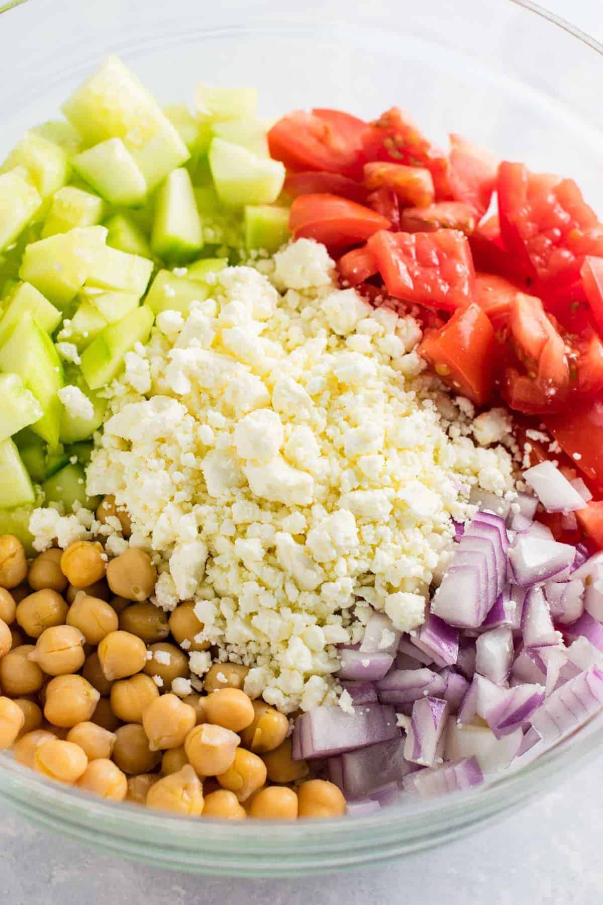 ingredients in a bowl before mixing - cucumbers, feta cheese, red onion, tomatoes, and chickpeas