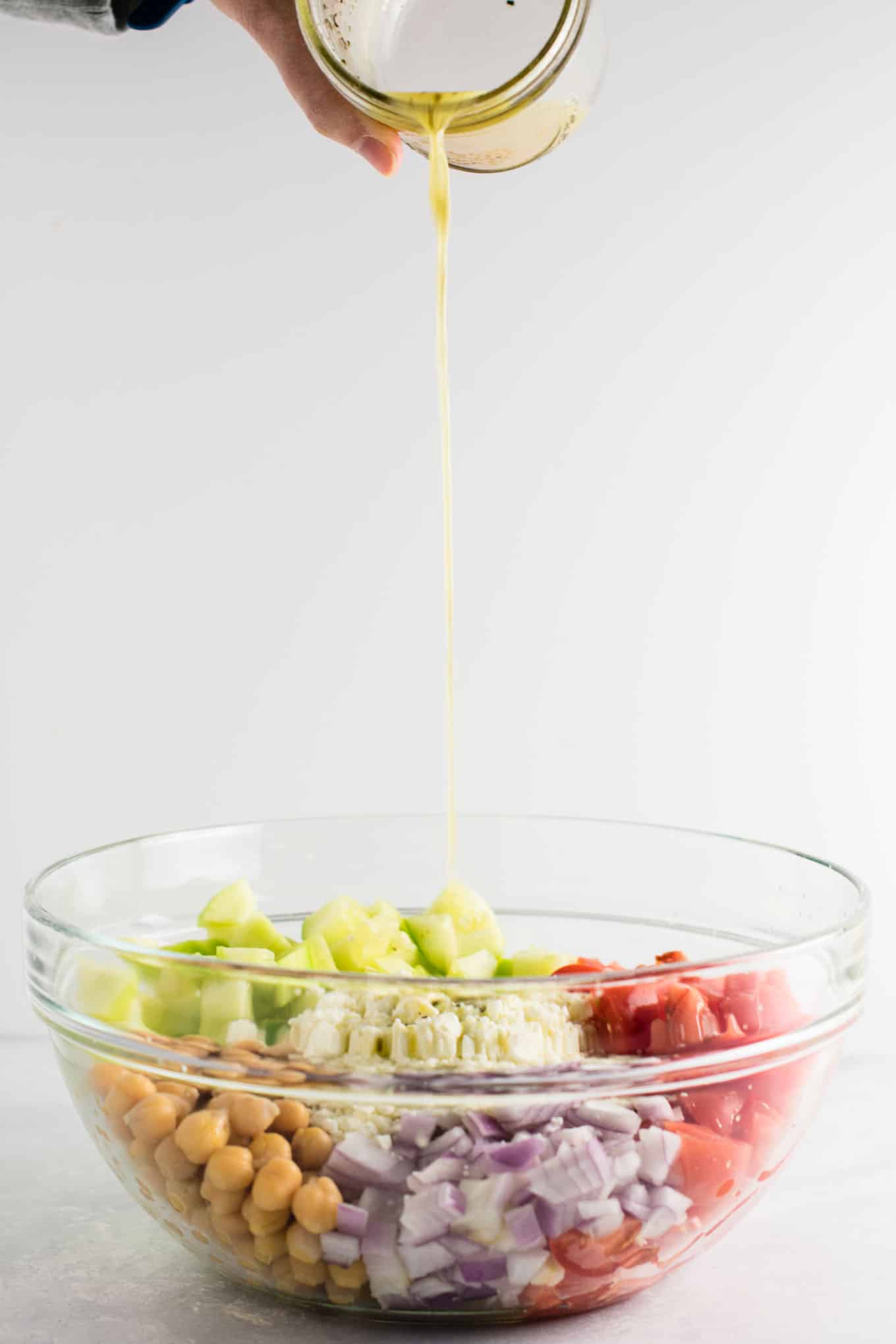 dressing being poured onto the greek salad