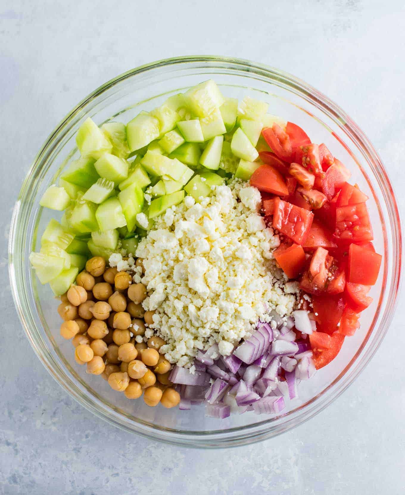 ingredients in a bowl before mixing - cucumbers, feta cheese, red onion, tomatoes, and chickpeas