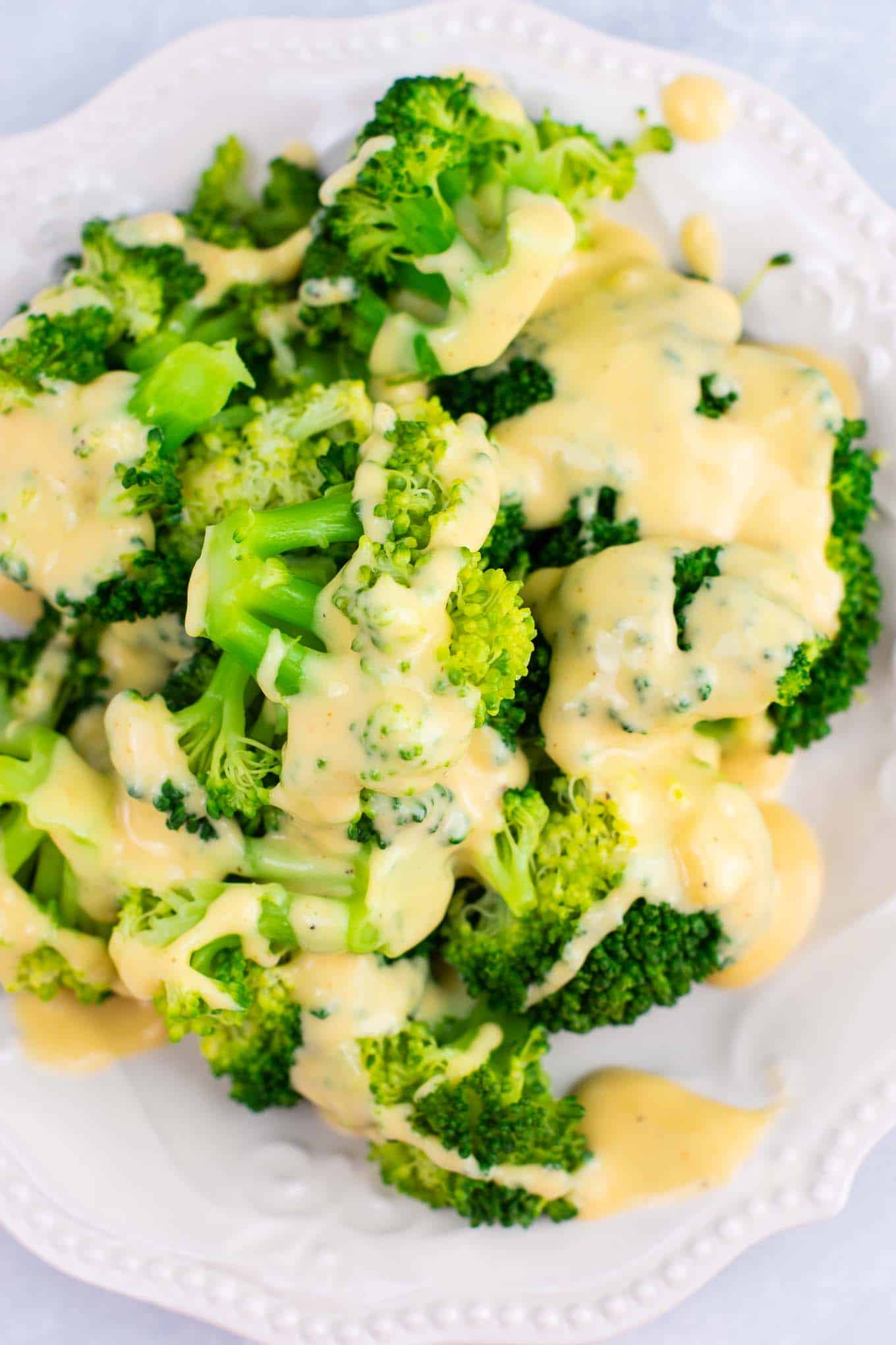 cheese sauce poured over broccoli on a white plate