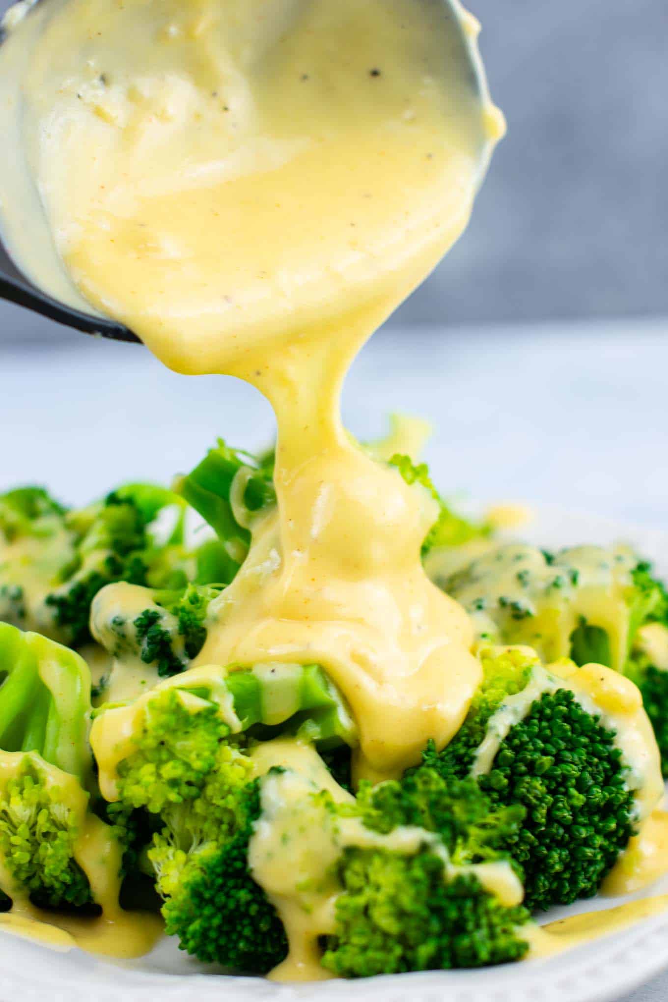 cheese sauce being poured over broccoli