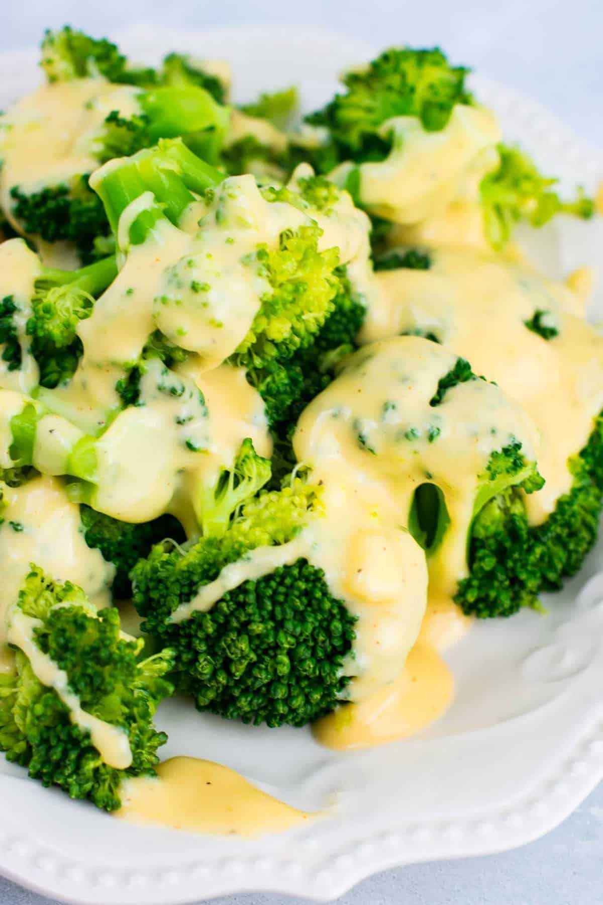 cheese sauce poured over broccoli on a white plate