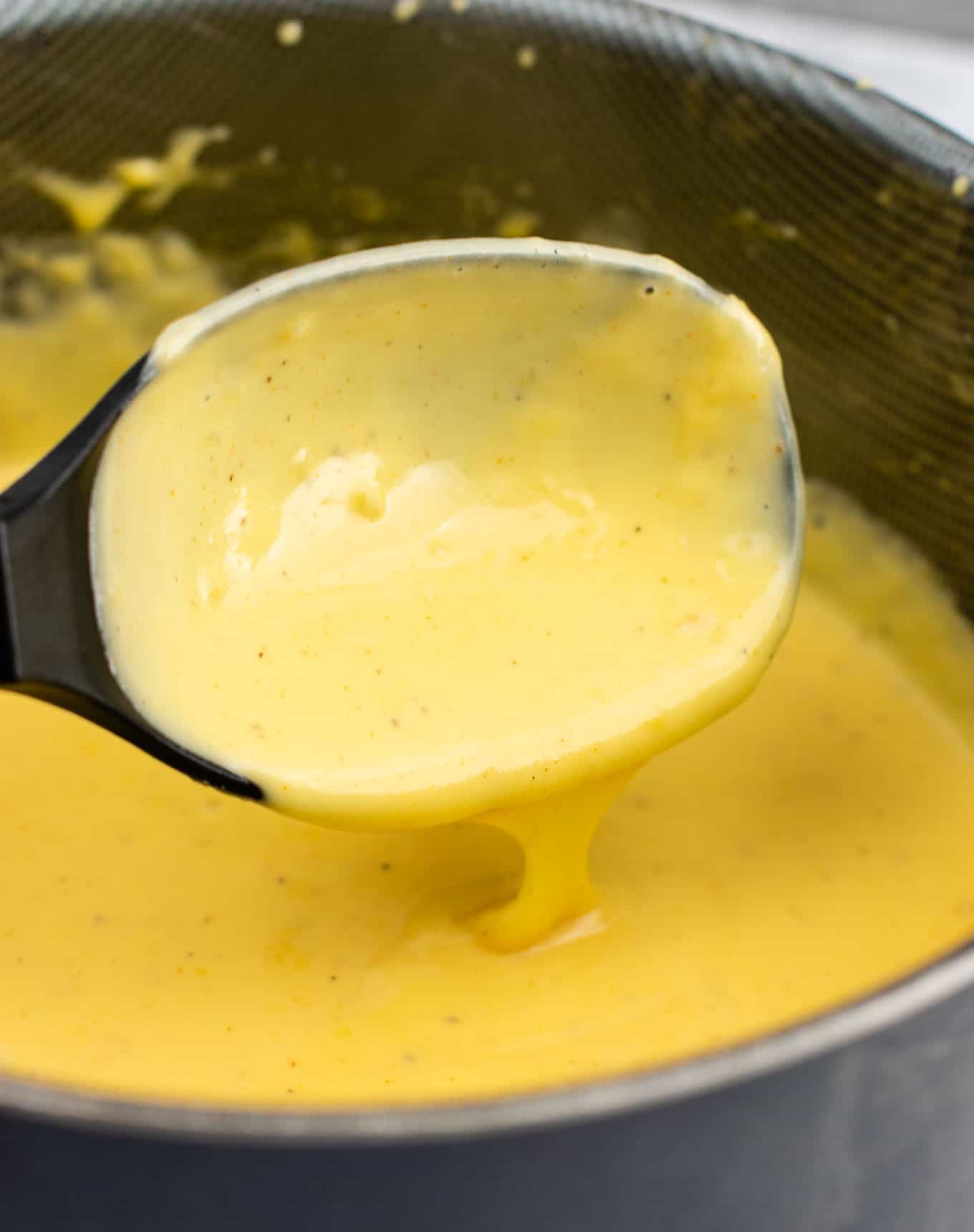 a spoon dripping with cheese sauce over a sauce pan