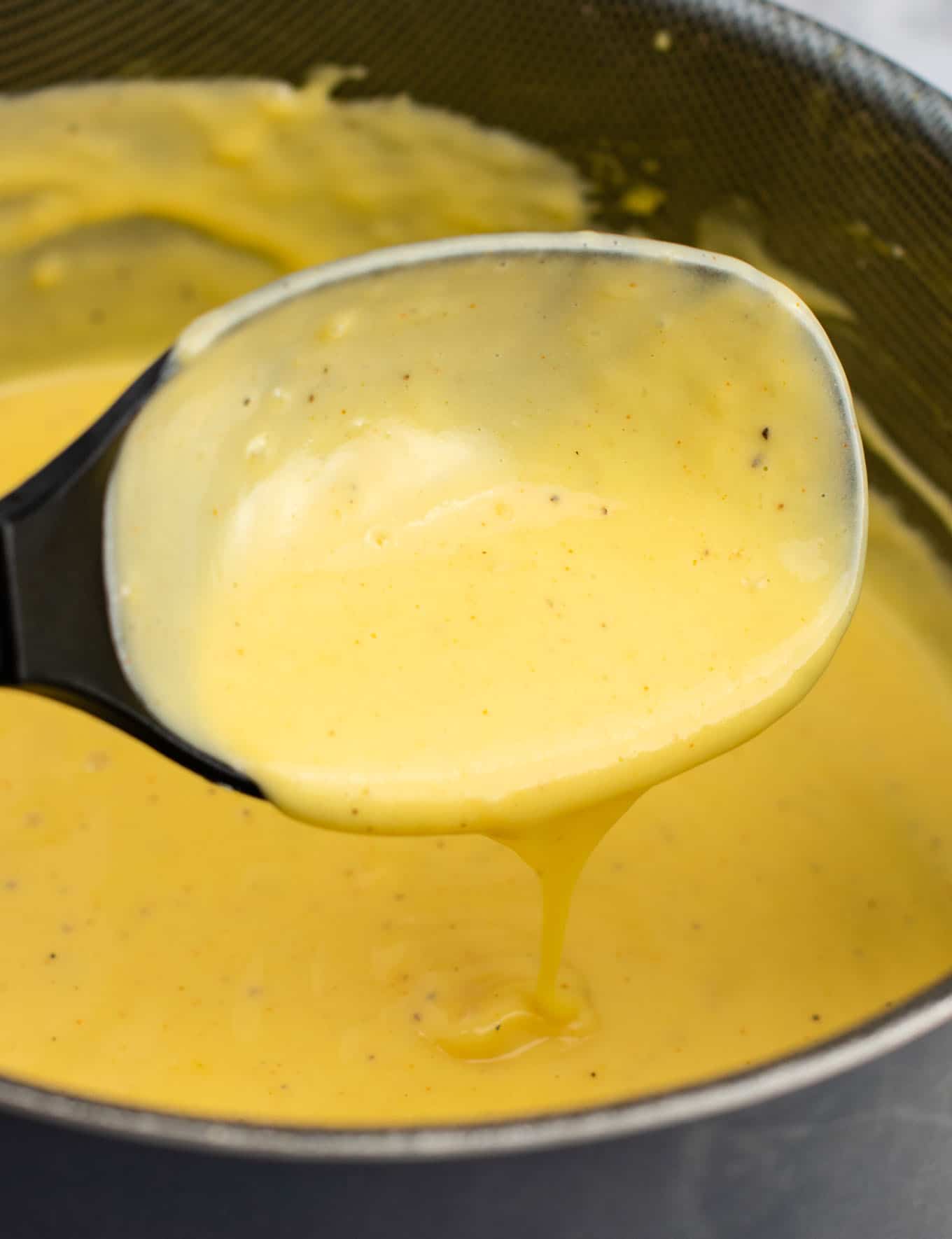 a spoon dripping cheese sauce into a sauce pan