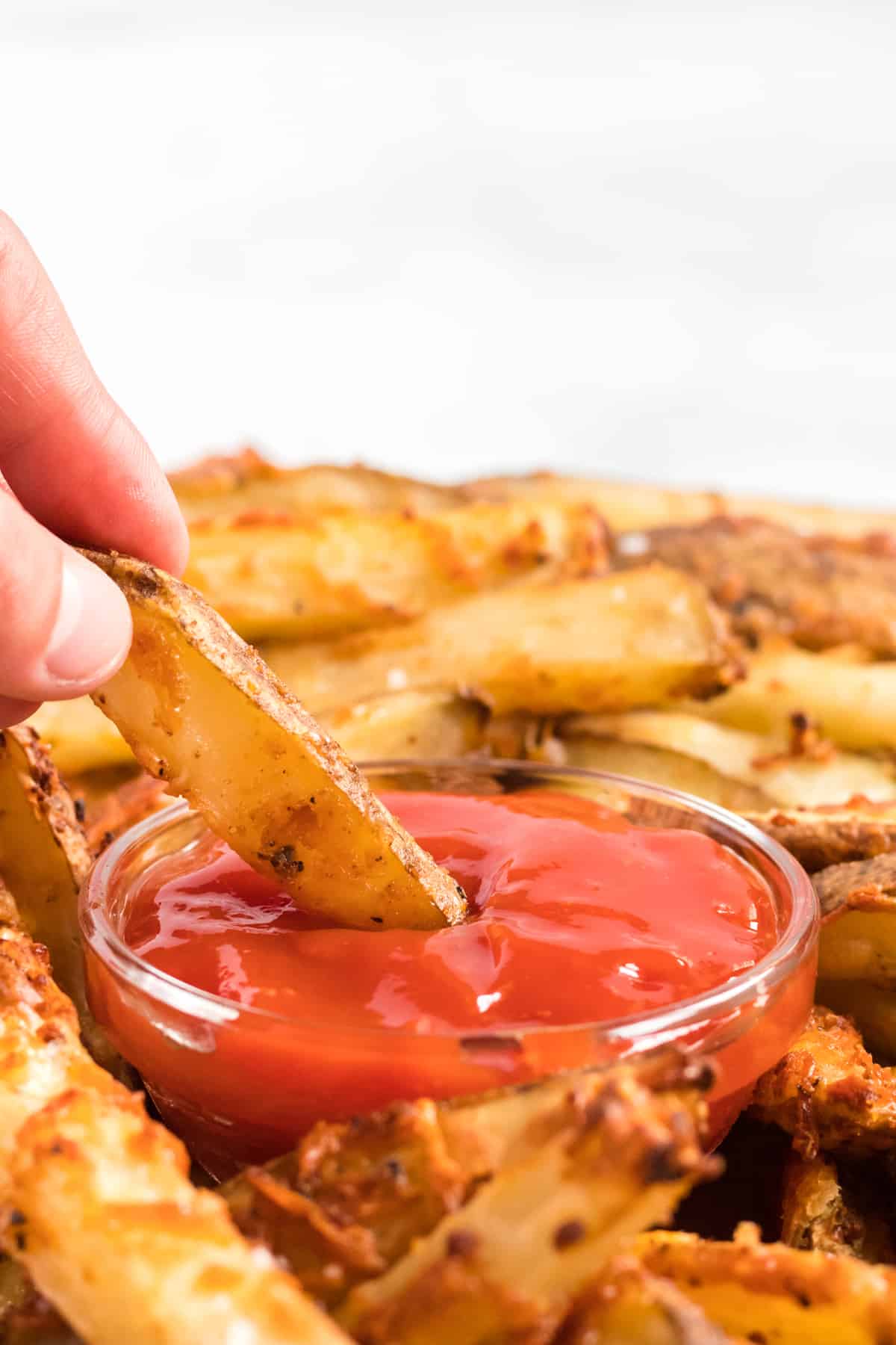 a parmesan crusted potato wedge being dipped in ketchup