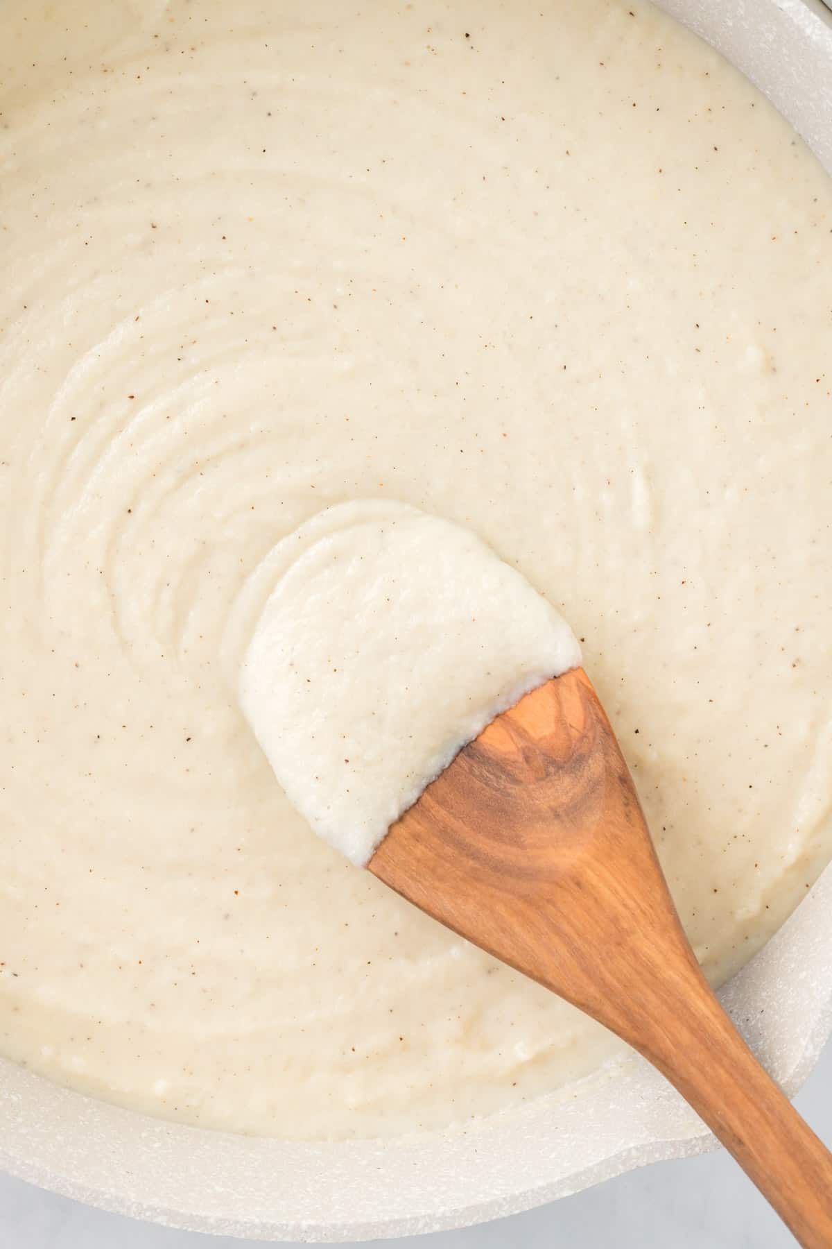 wooden spoon dipped in cauliflower alfredo sauce