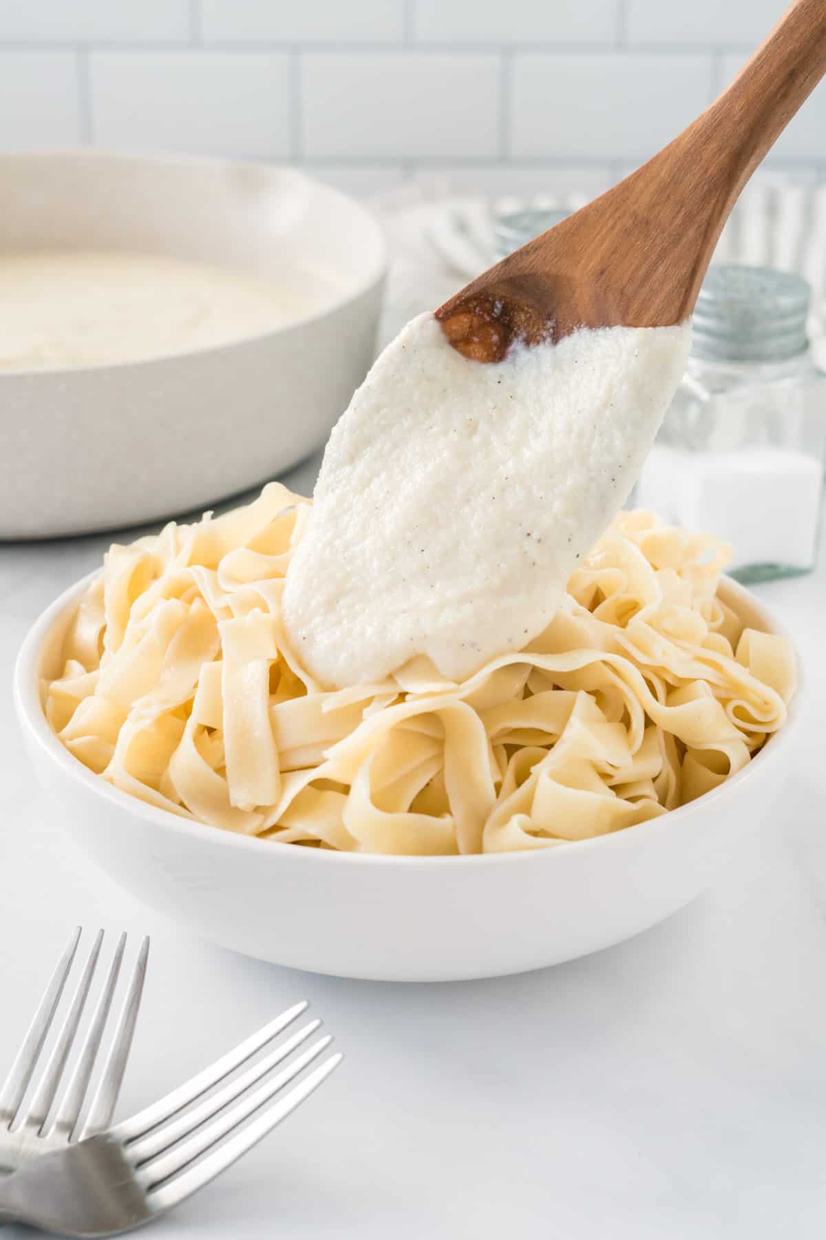 pouring cauliflower Alfredo sauce over a bowl of fettuccini noodles