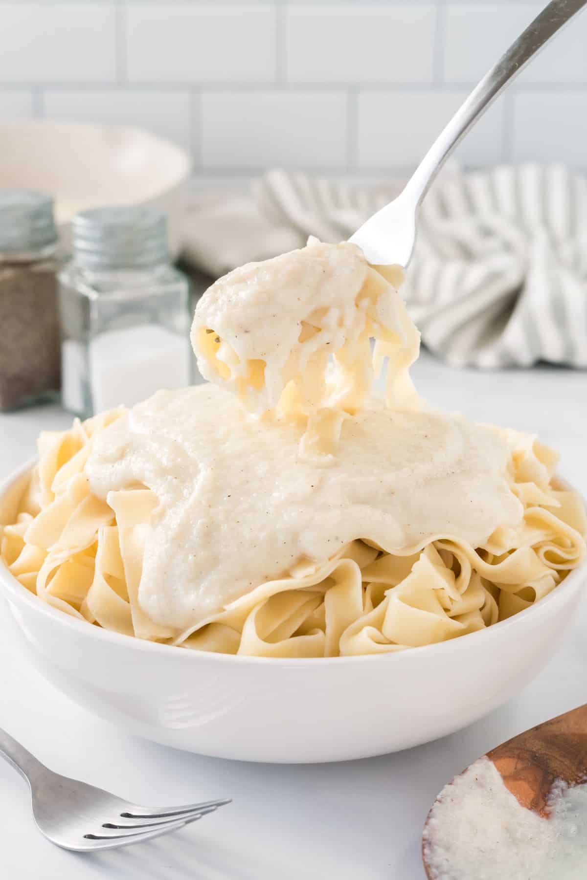 a fork taking a bite of fettuccini with Alfredo sauce