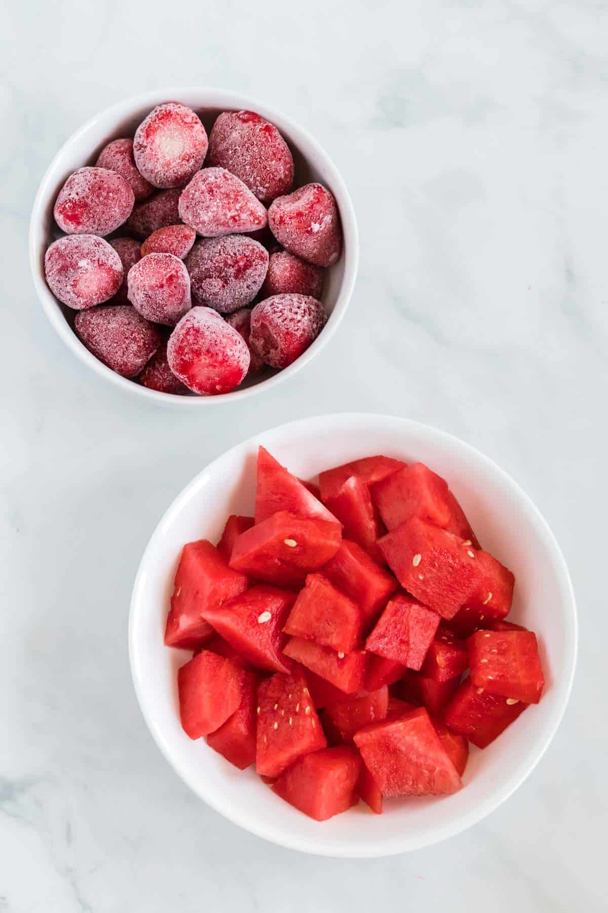 fresh watermelon and frozen strawberries in white bowls