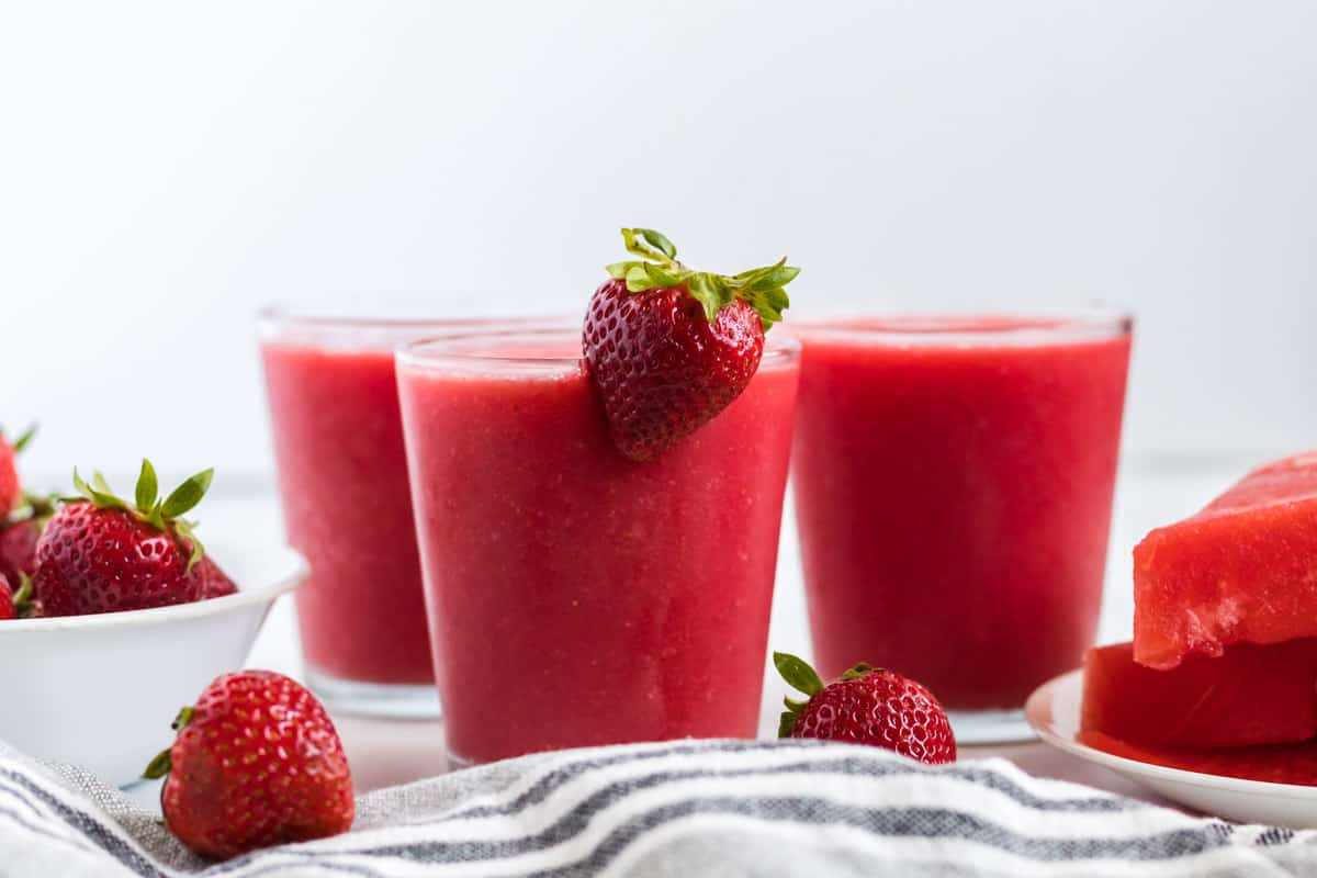 strawberry watermelon smoothie in a clear glass with a strawberry on the rim