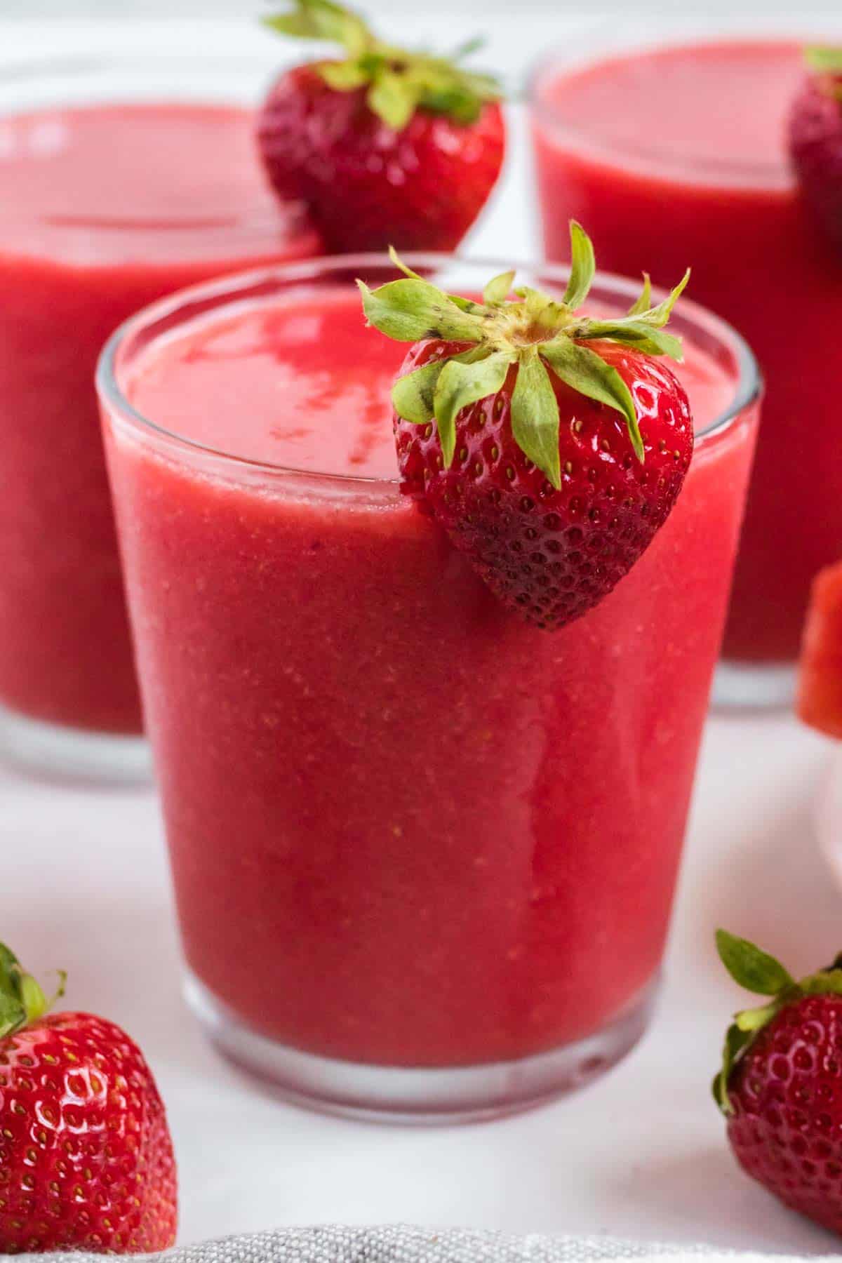 strawberry watermelon smoothie in a clear glass with a strawberry on the rim