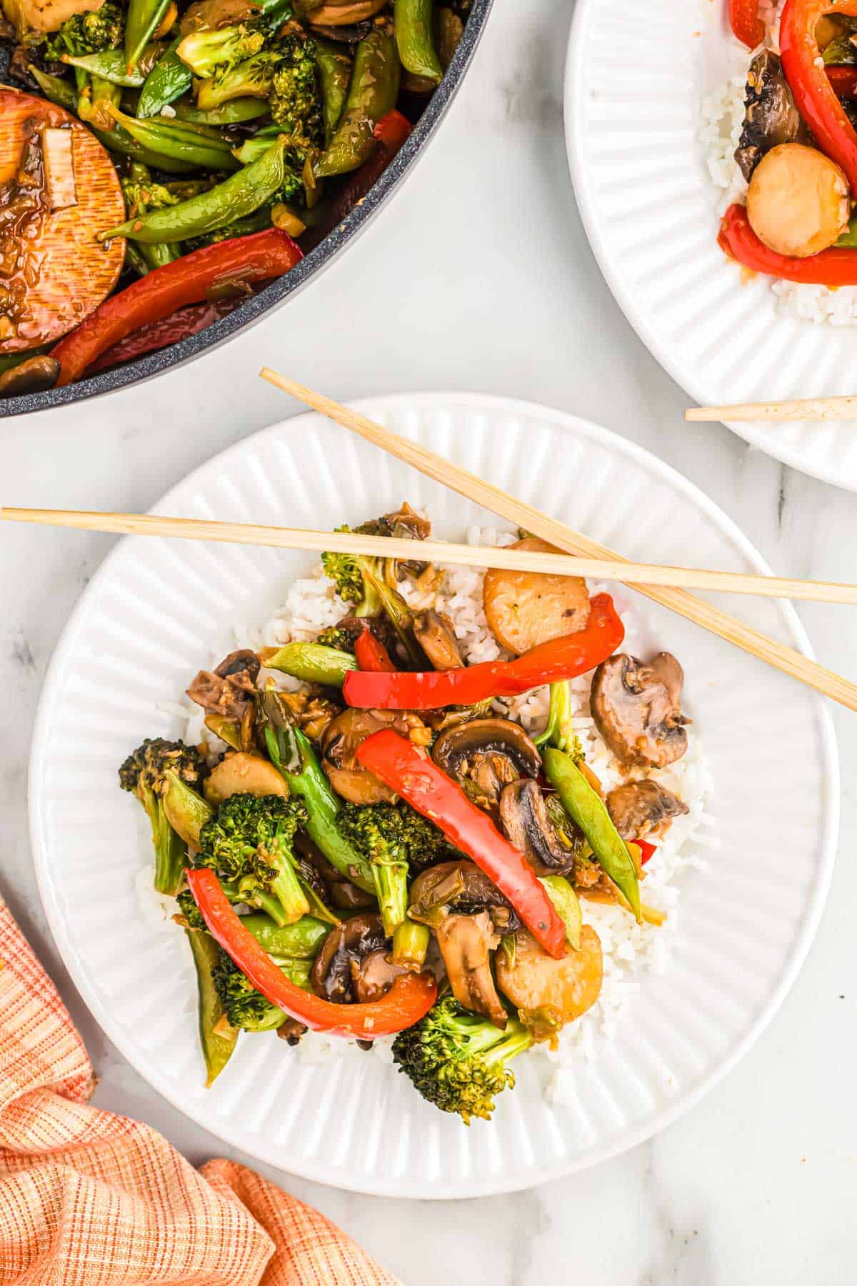 veggie stir fry over white rice on a plate with chopsticks