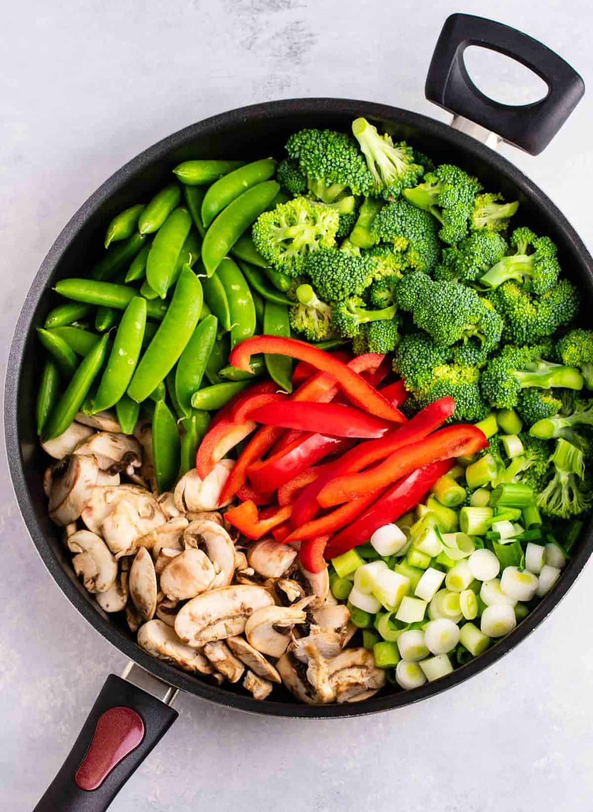 a skillet with stir fry veggies - snap peas, broccoli, red bell pepper, green onion, and sliced mushrooms