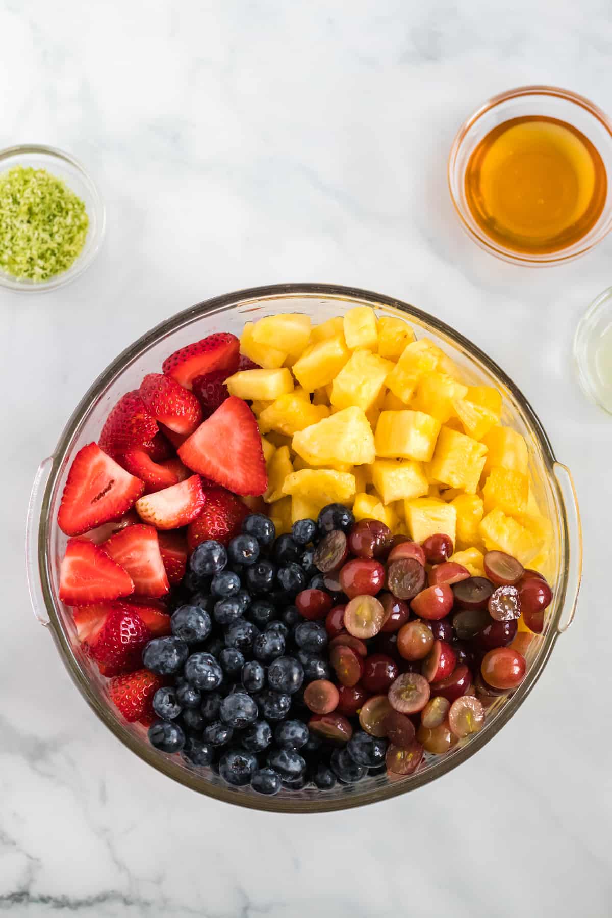 a large glass bowl with the prepared strawberries, blueberries, grapes, and pineapple in it