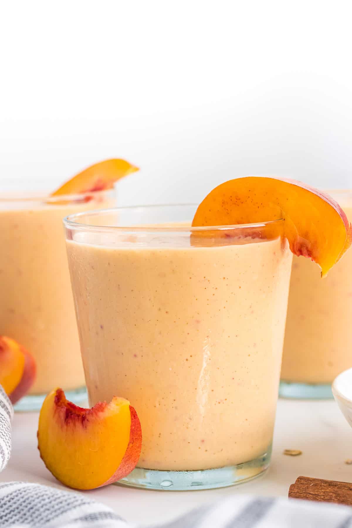 healthy peach smoothie in a glass with a peach slice on the rim