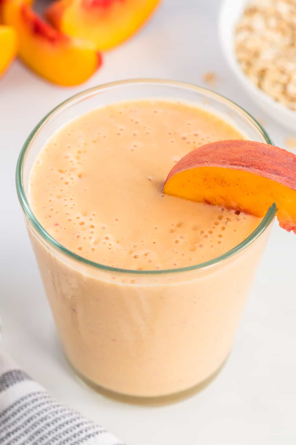 healthy peach smoothie in a glass with a peach slice on the rim