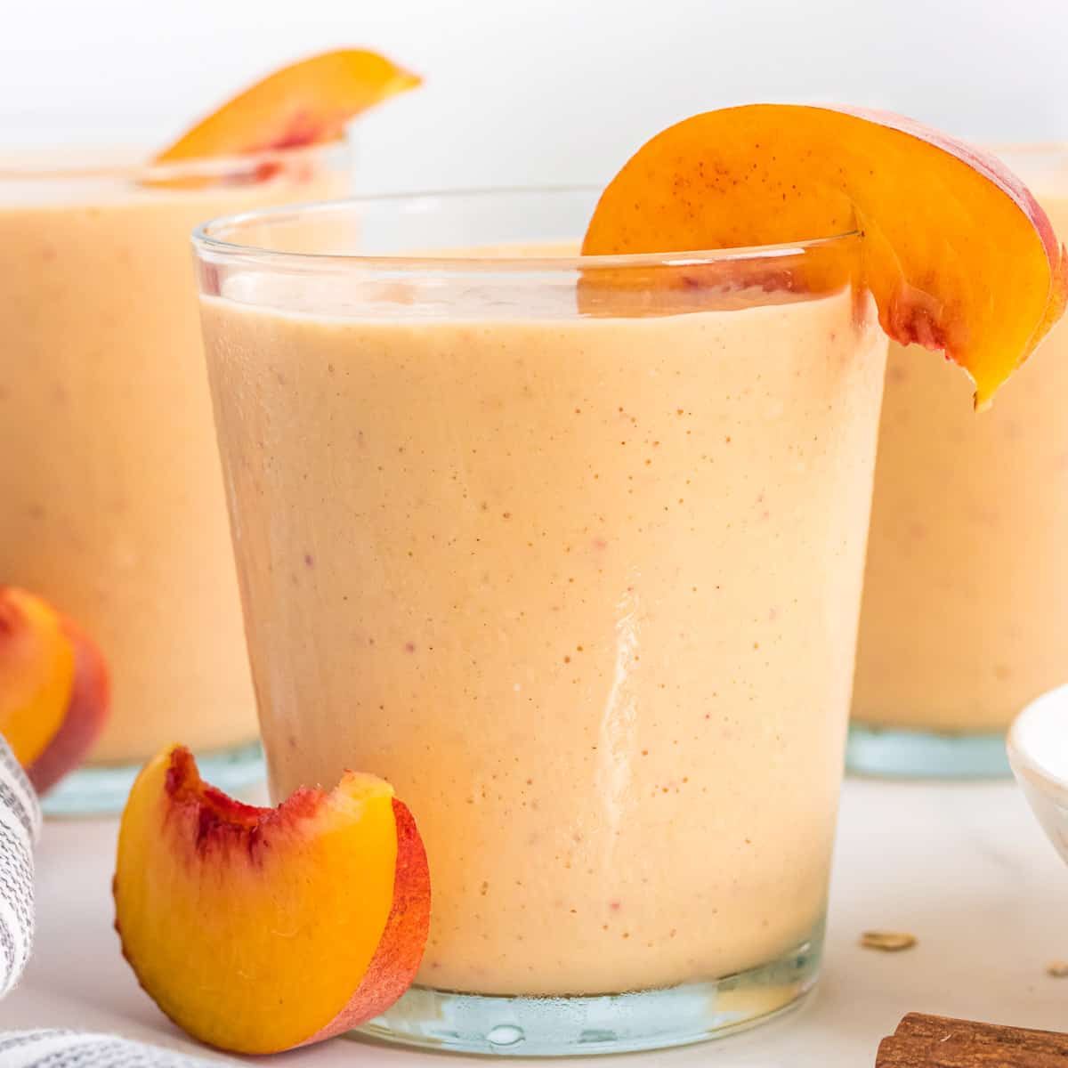 healthy peach smoothie in a glass with a peach slice on the rim