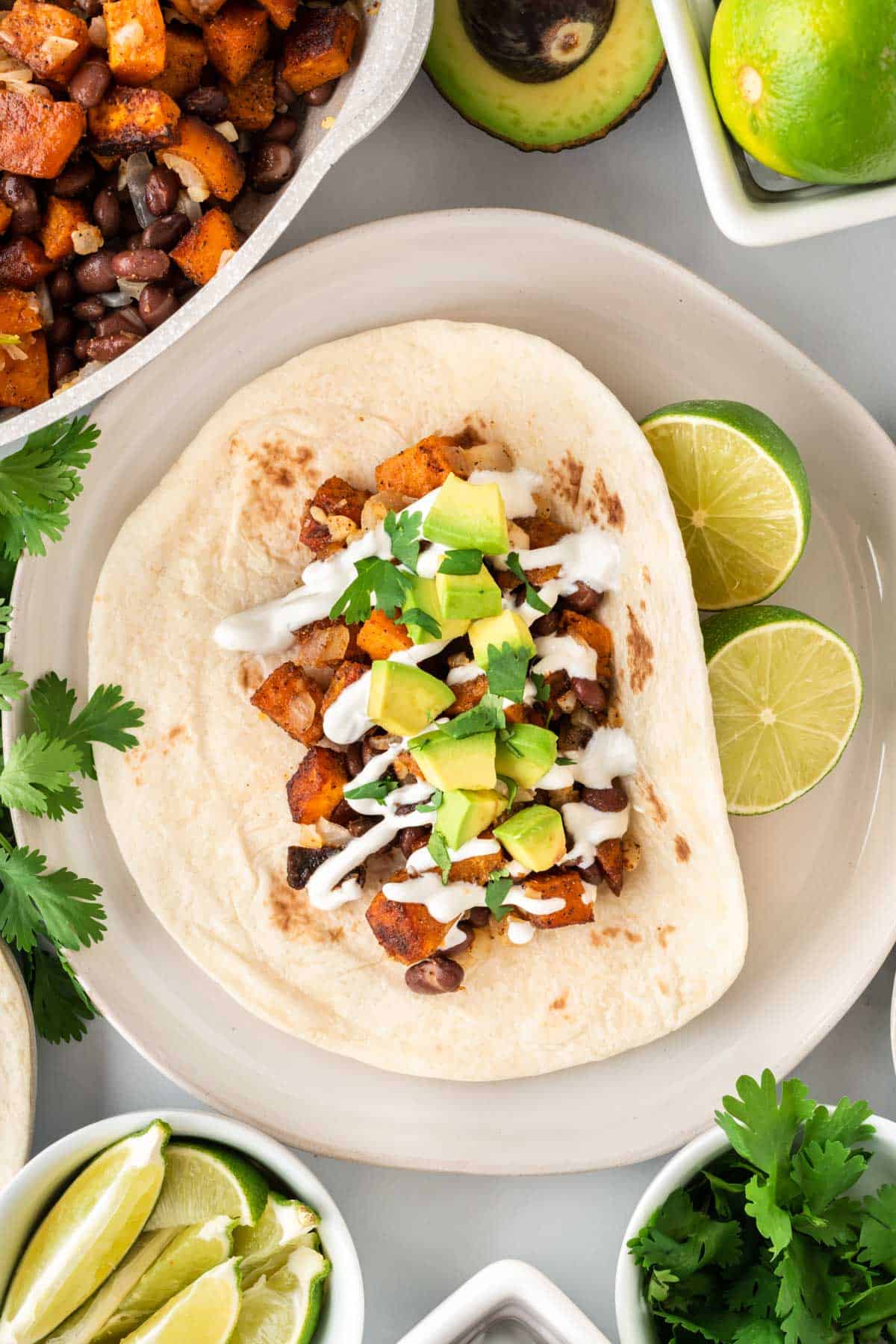 open faced black bean sweet potato taco on a plate topped with sour cream, cilantro, and avocado