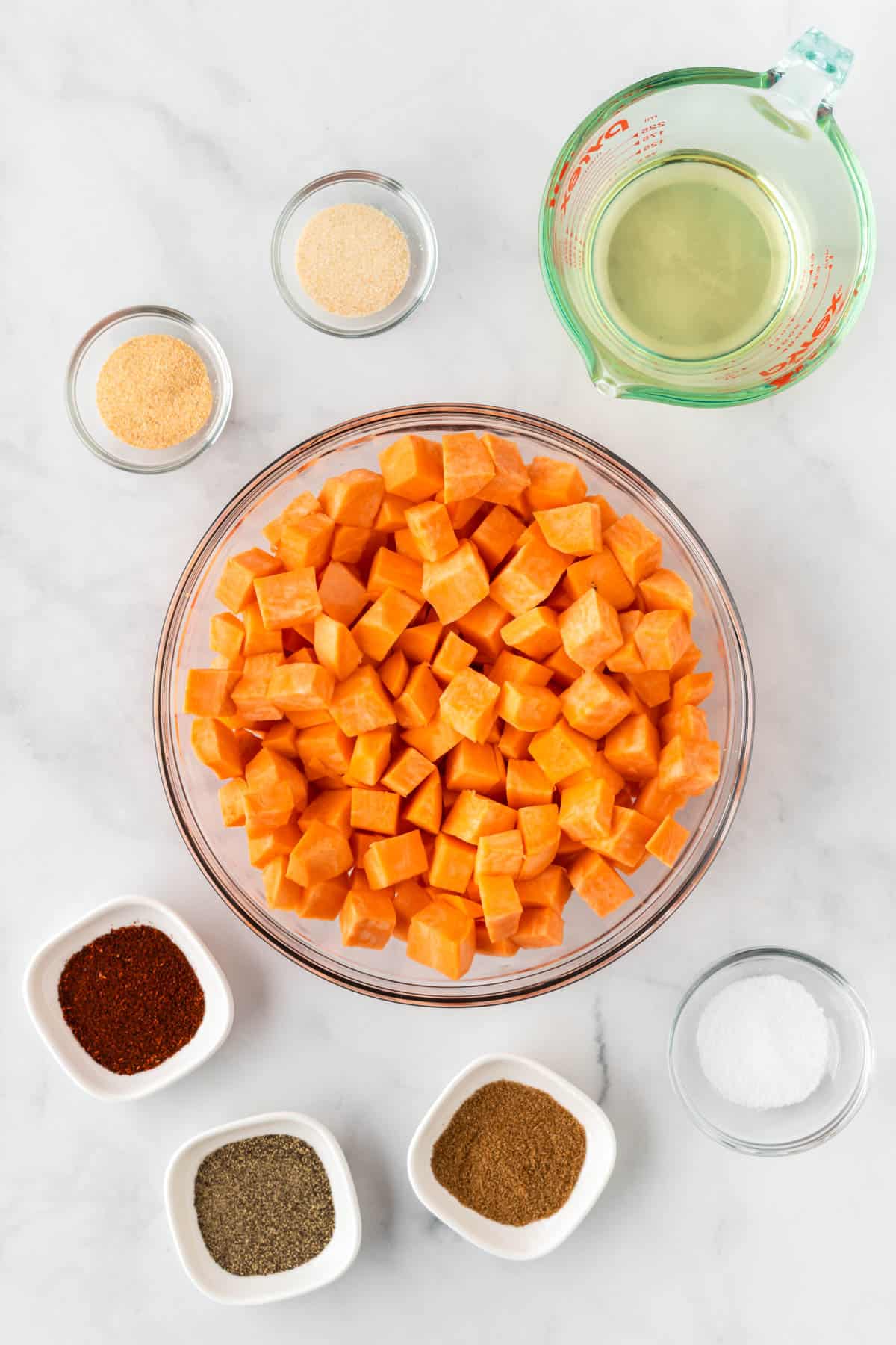 diced sweet potatoes in a bowl surrounded by oil and spices