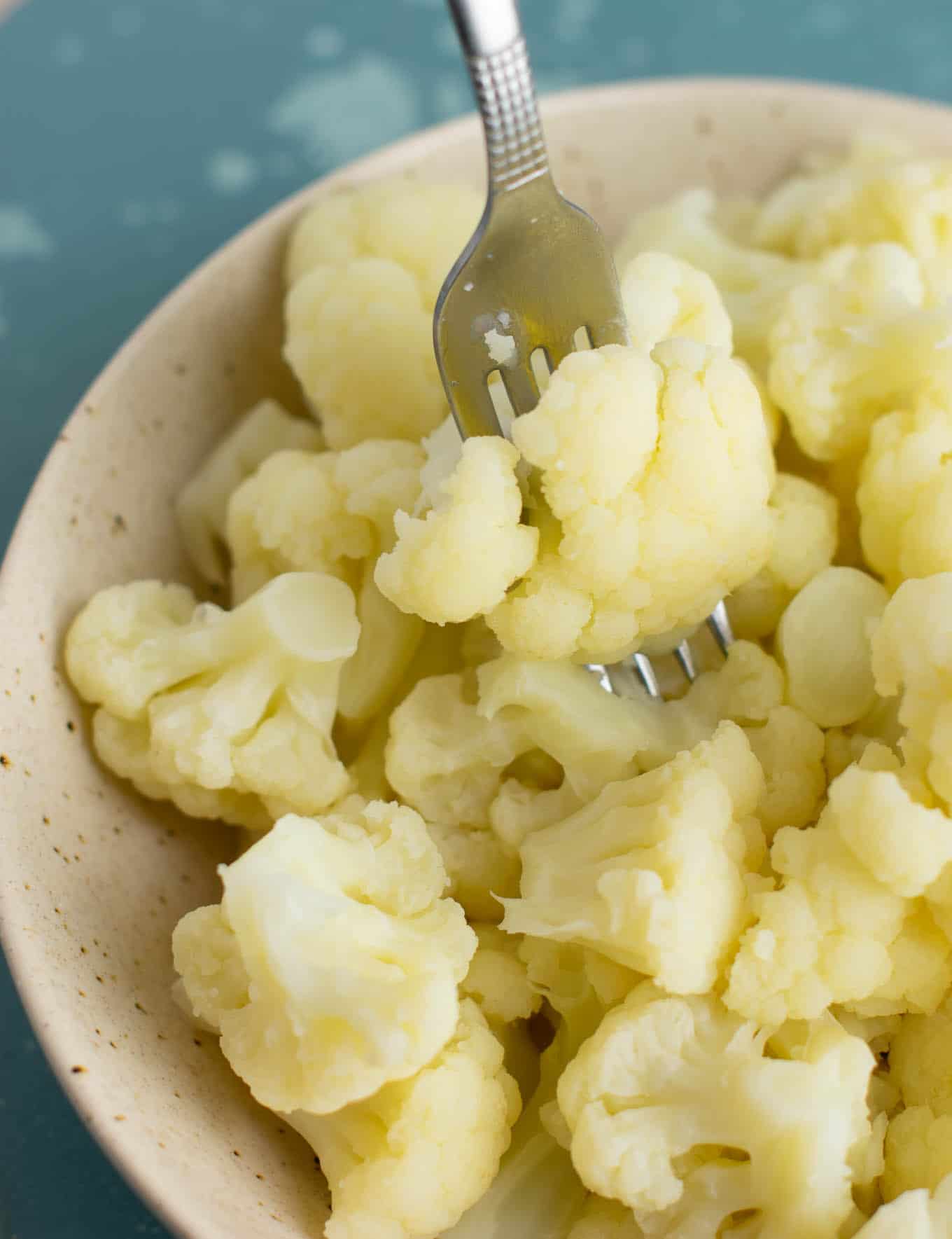 a fork taking a piece of steamed cauliflower from the bowl