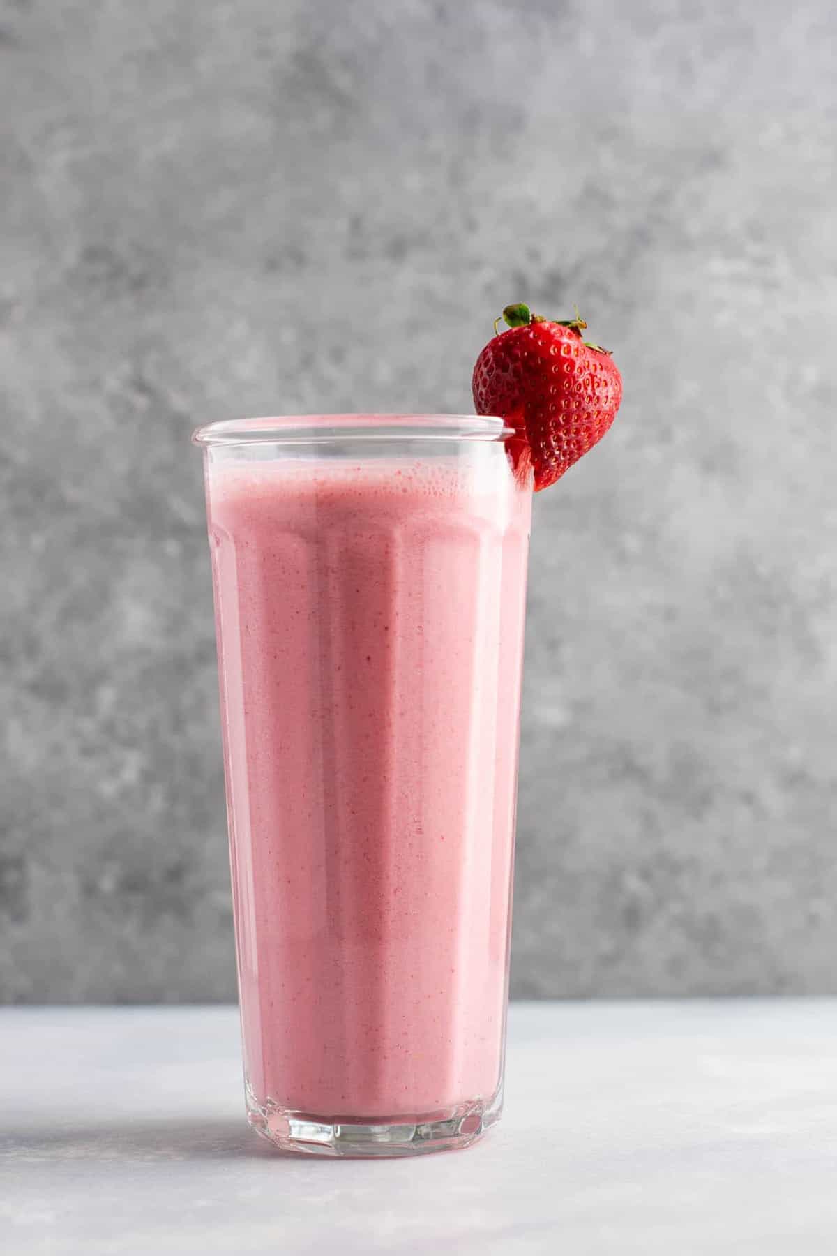 Strawberry smoothie in a tall glass with a strawberry on the rim